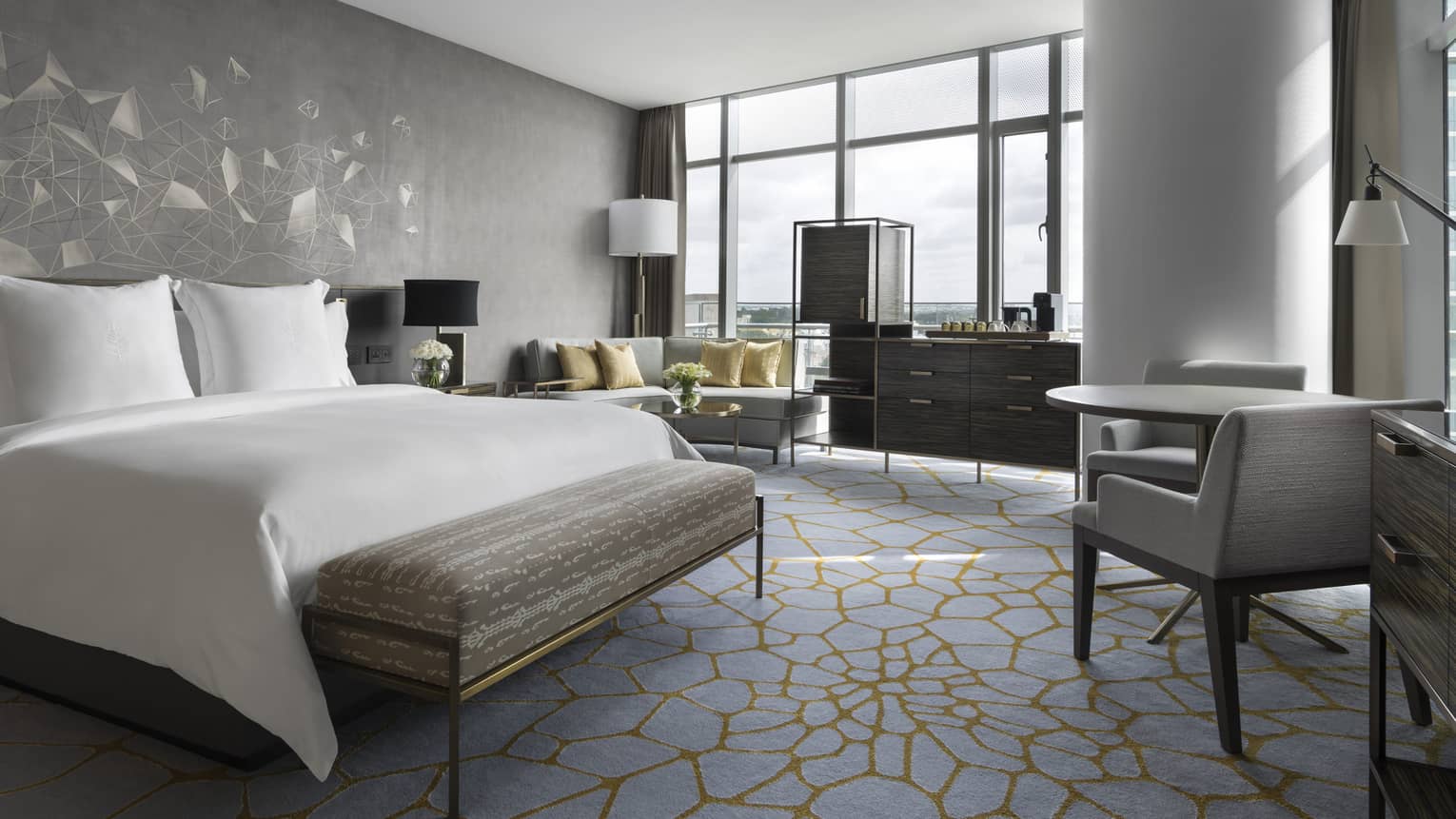 Deluxe room with queen bed, white linens, small table for 2, couch, floor-to-ceiling windows 