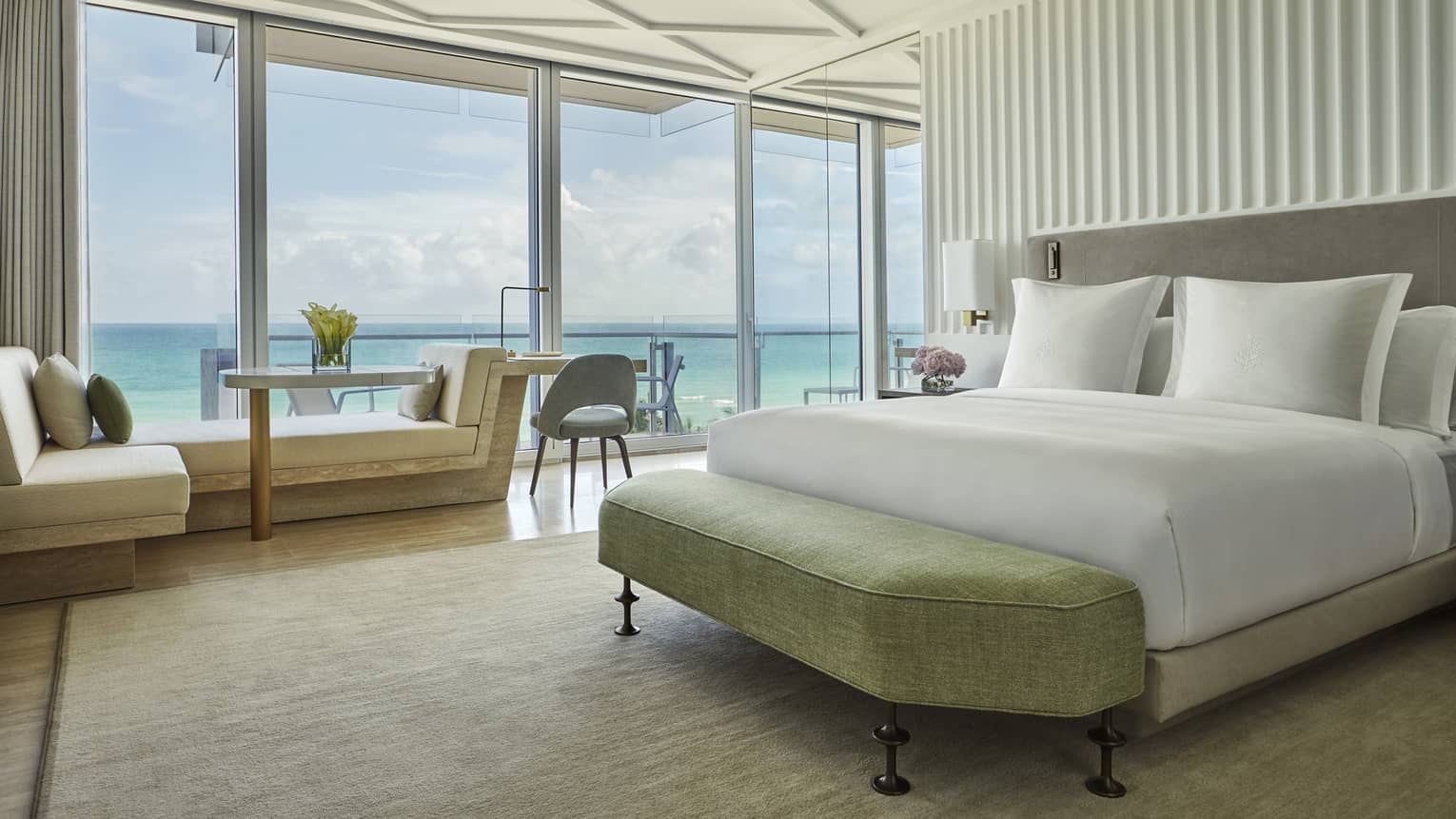 Luxurious beachside suite with white wedding, sofa, floor-to-ceiling windows overlooking patio and ocean views