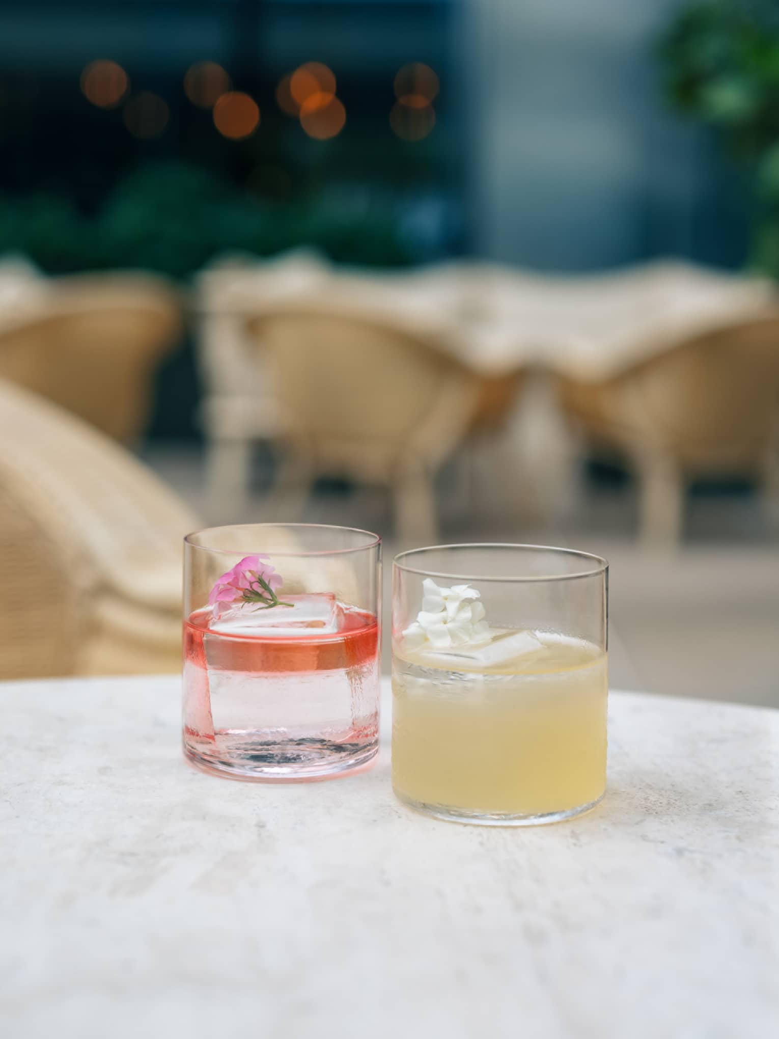 Two cocktails served in rocks glasses sit side by side on a white marble table
