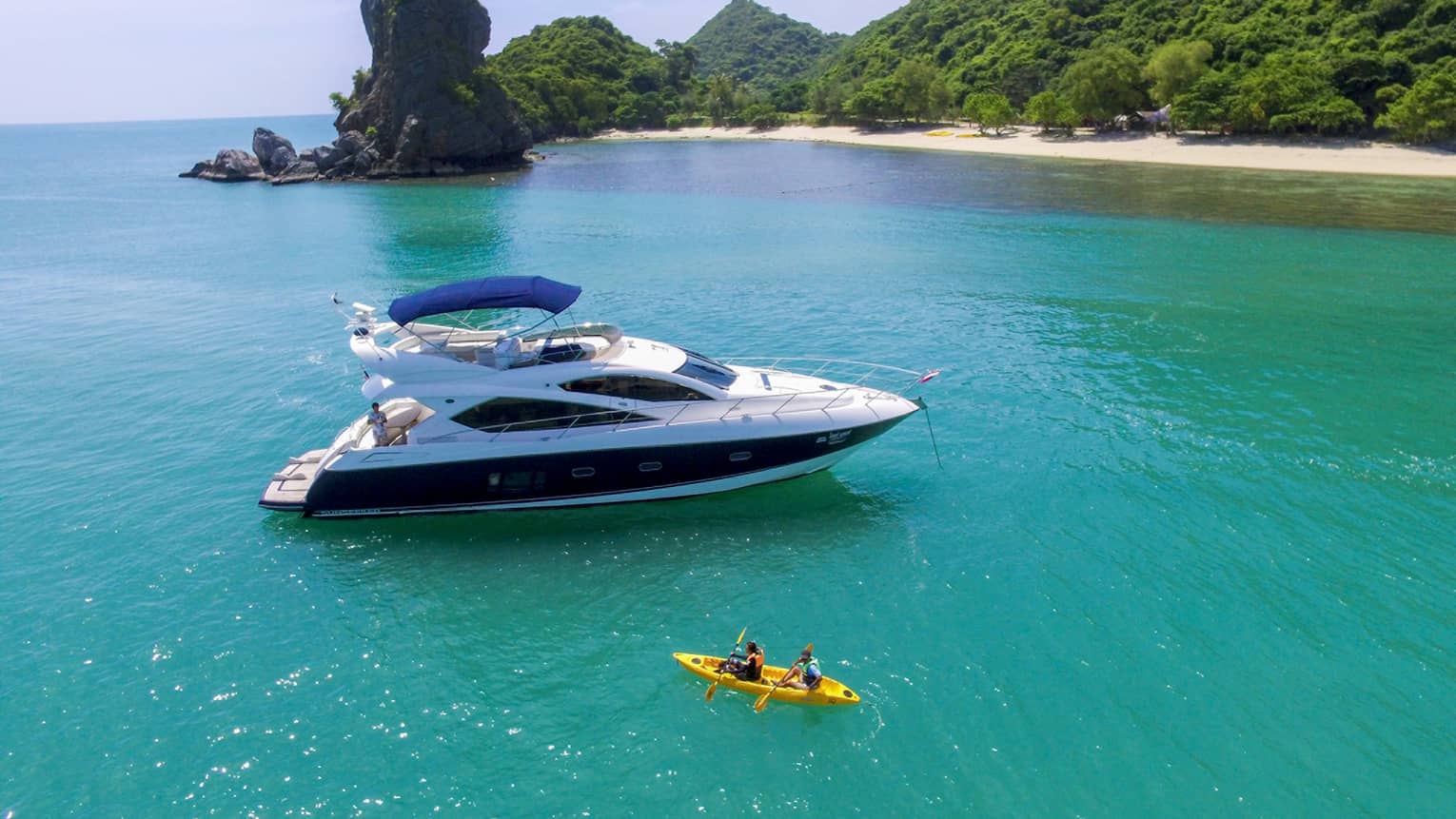 Two people in yellow kayak in front of large white yacht by island in blue ocean