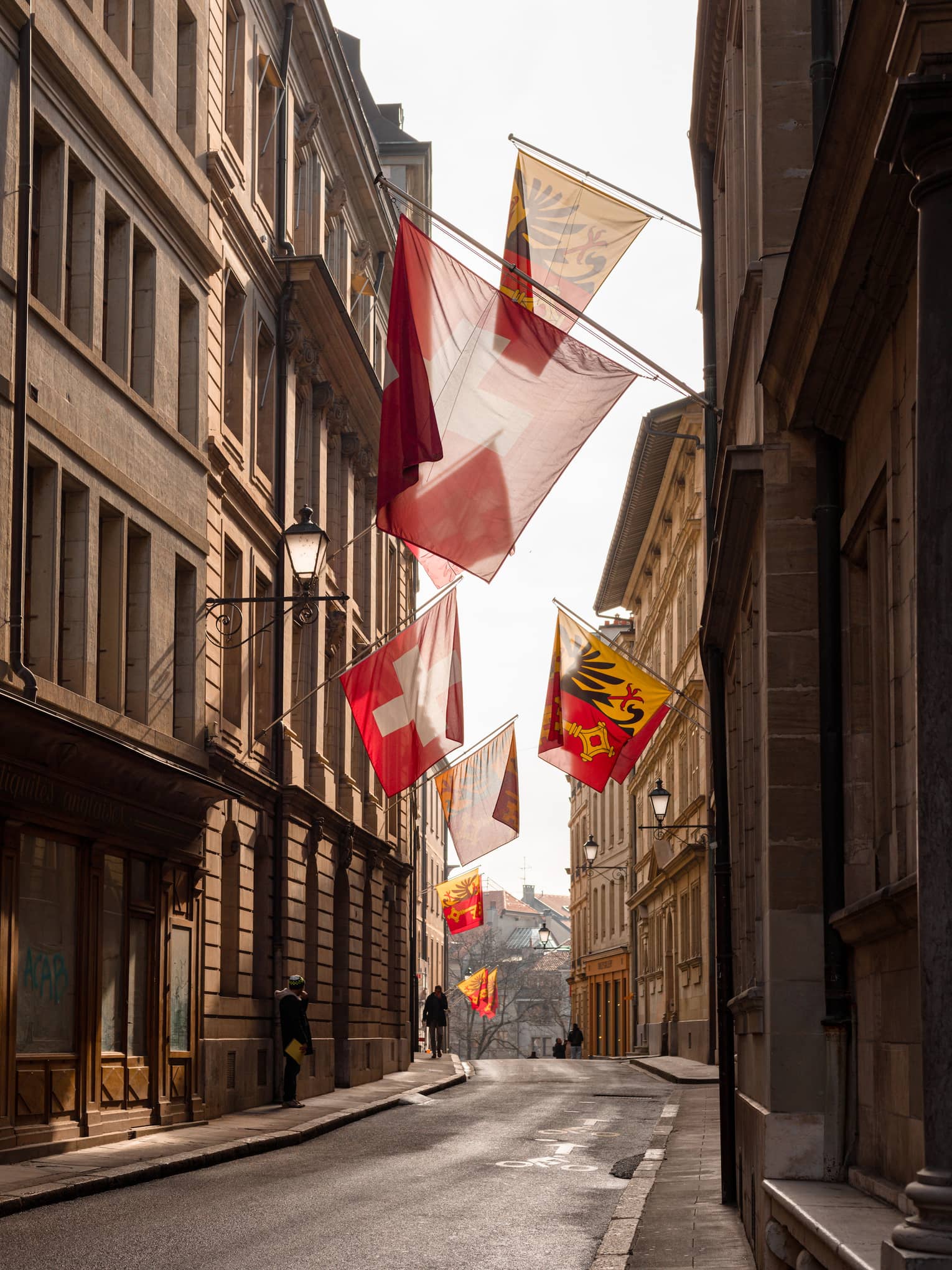 Narrow street in Old Town Geneva lined by Swiss flags hanging from the walls of the traditional buildings. 