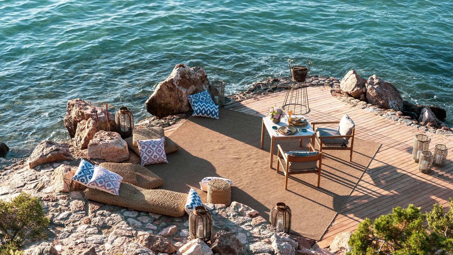 A dining table with two chairs is set on a private rocky peninsula next to the sea