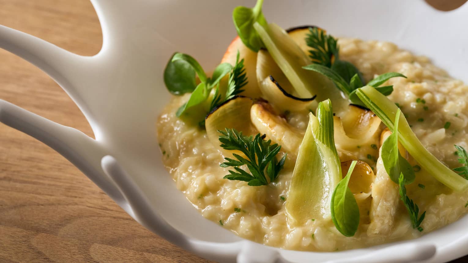 An artistic white bowl with an amorphous edge holds a rice dish with bright green garnishes.