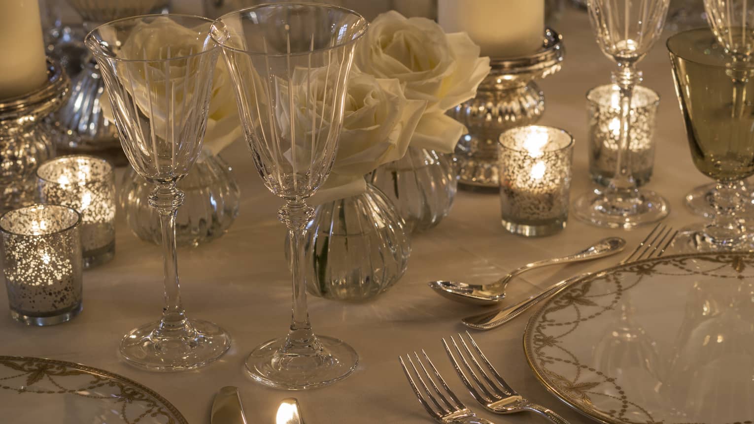 Crystal glasses, dishes with gold accents, glowing candles on wedding banquet table