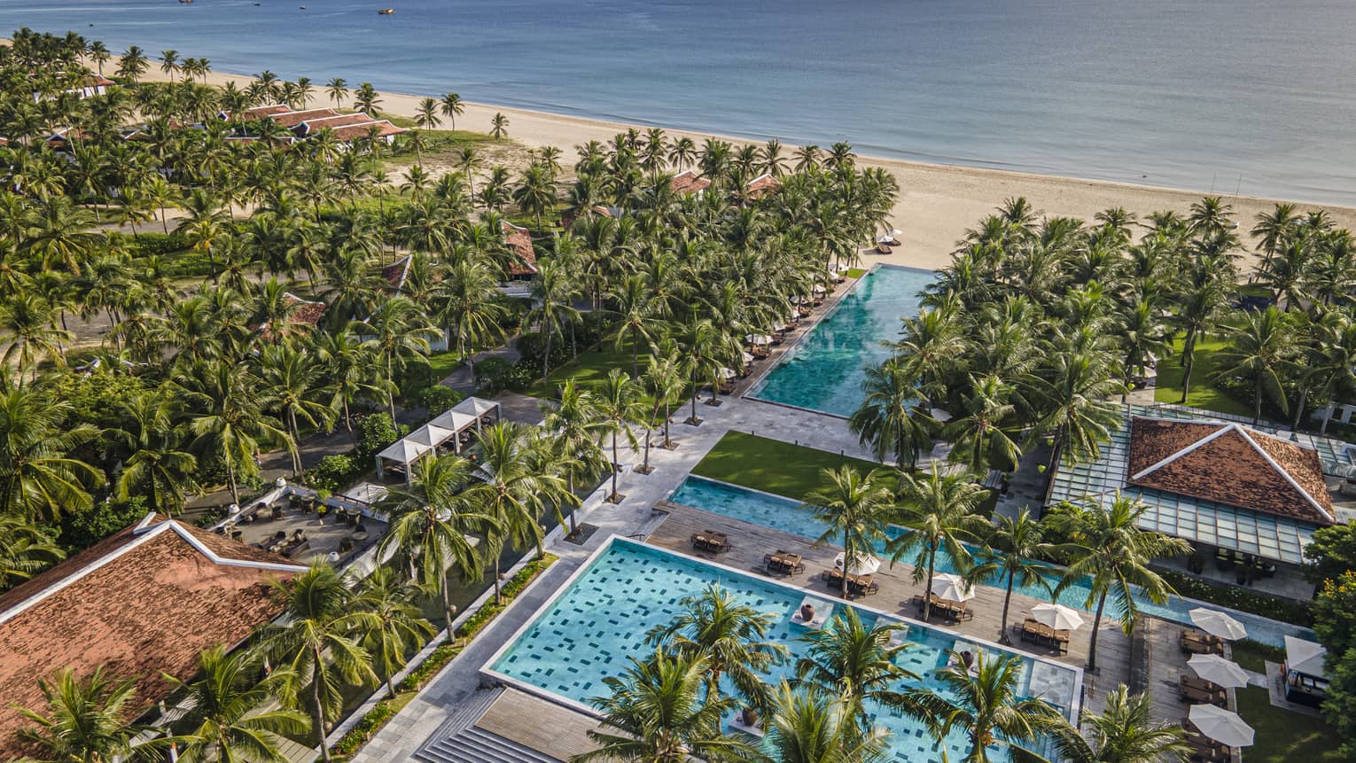 Aerial view of the resort pools with ocean views, palm trees and blue skies