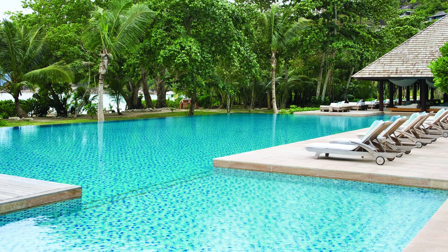 Row of white pool lounge chairs along side of swimming pools, palm trees in background