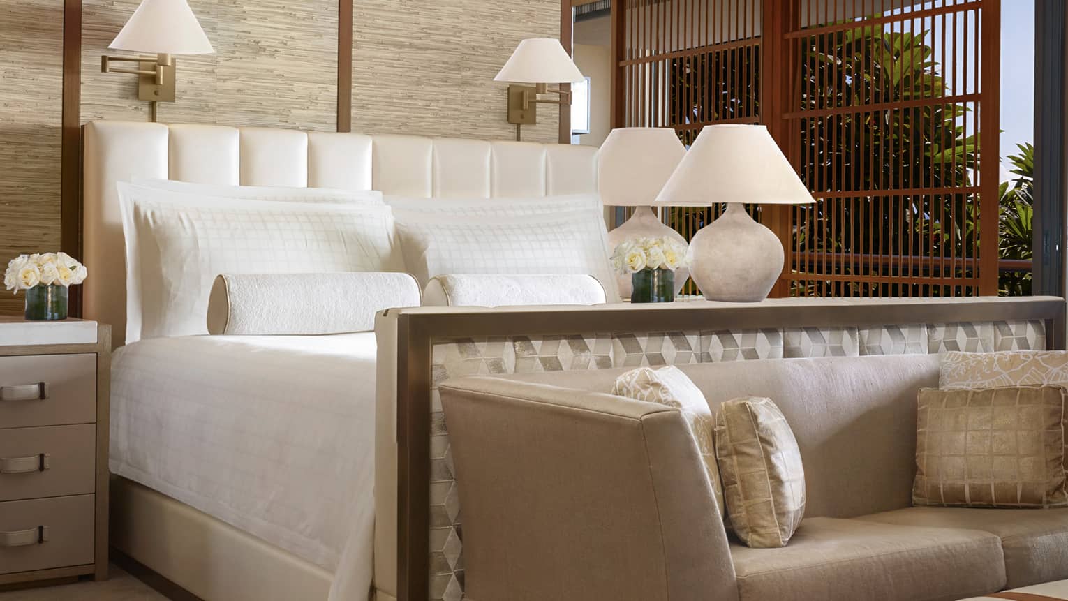 Makai Suite hotel bed, dresser with white flowers, lamp, small plush sofa and silk pillows at foot