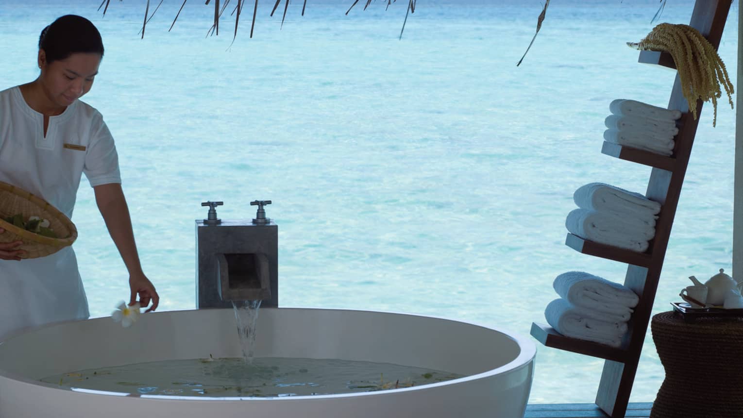 Spa & Ayurvedic Retreat staff places flowers in free standing tub on patio over lagoon