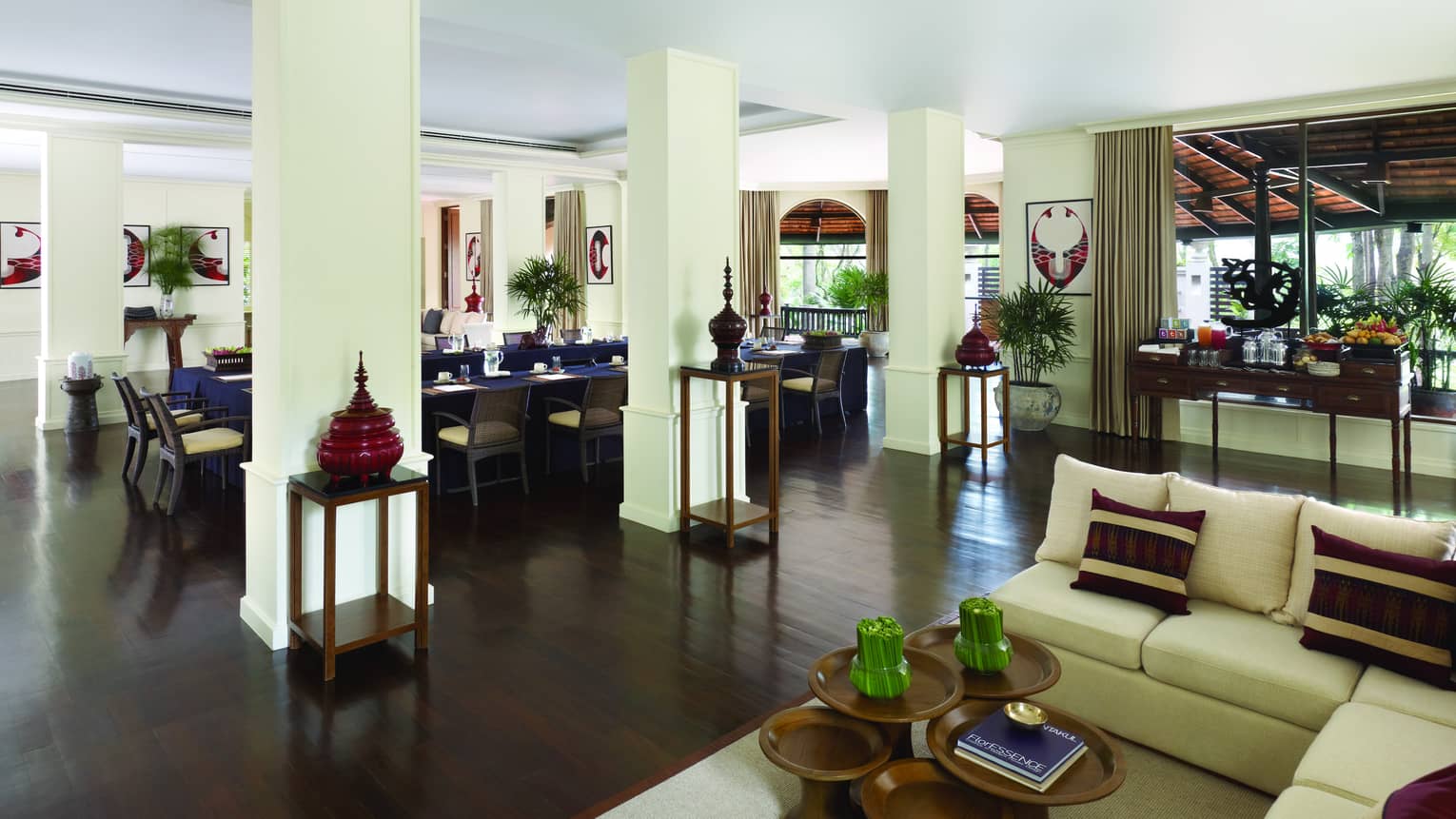 Seating area with sofa, small wood tables by white pillars before dining room
