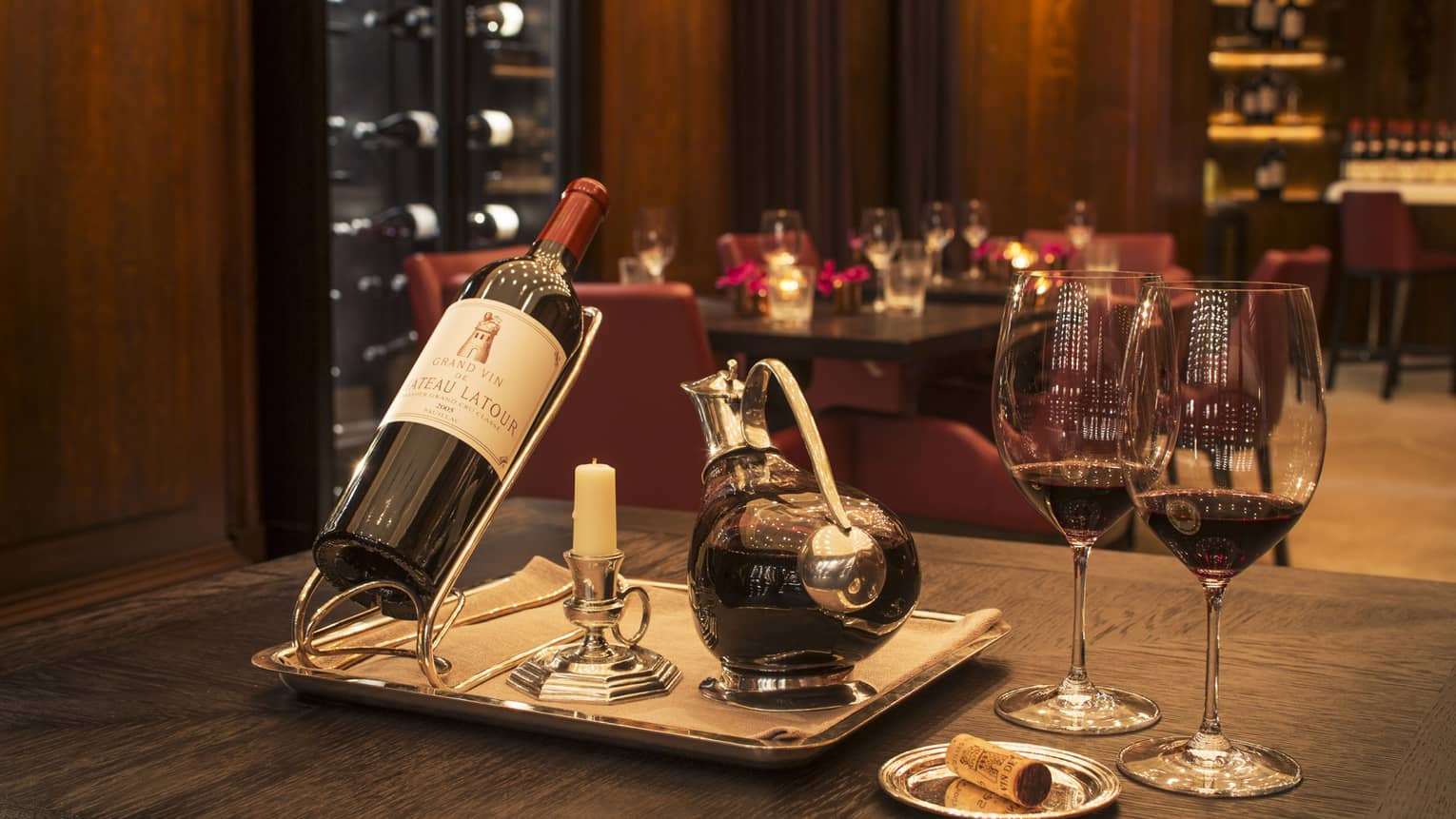 A bottle of red wine, a decanter and two glasses in a dimly lit restaurant.