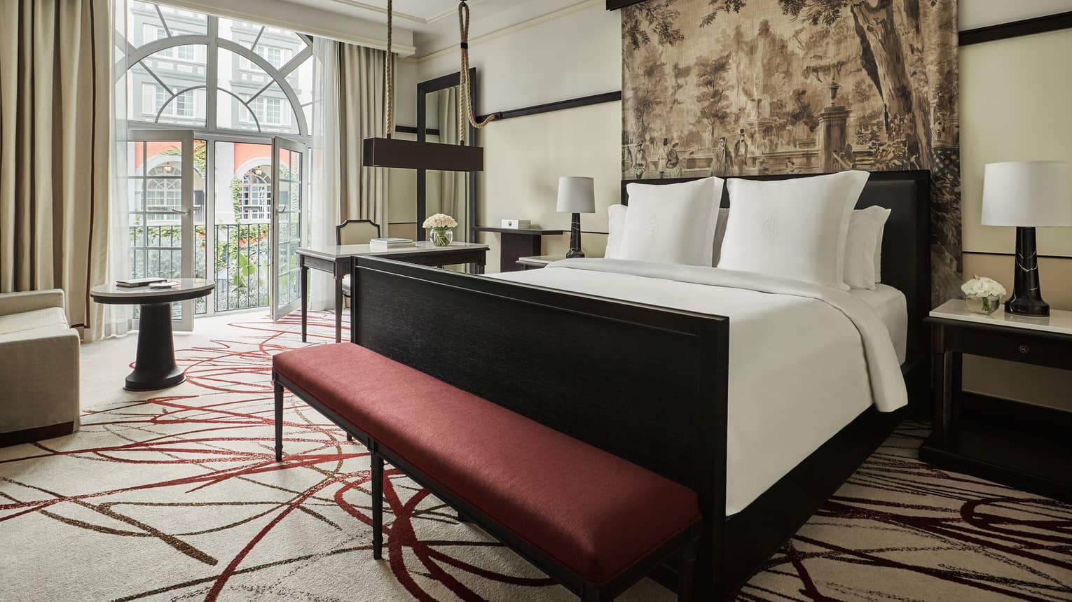 Premier Room bed under print headboard, red bench at foot, sunny arched balcony glass doors