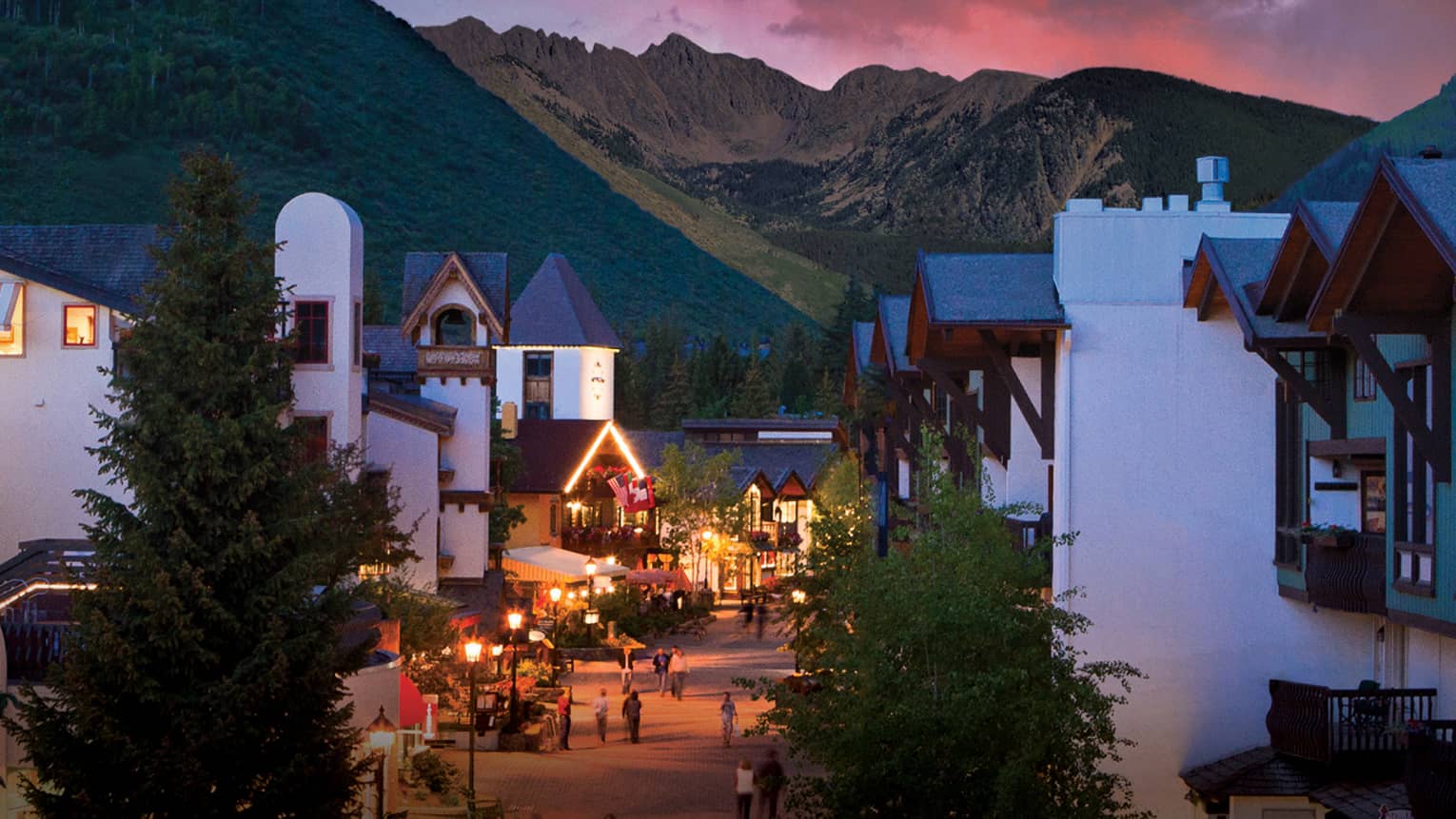A sunset over a small village like city center with white buildings and mountains in the distance.