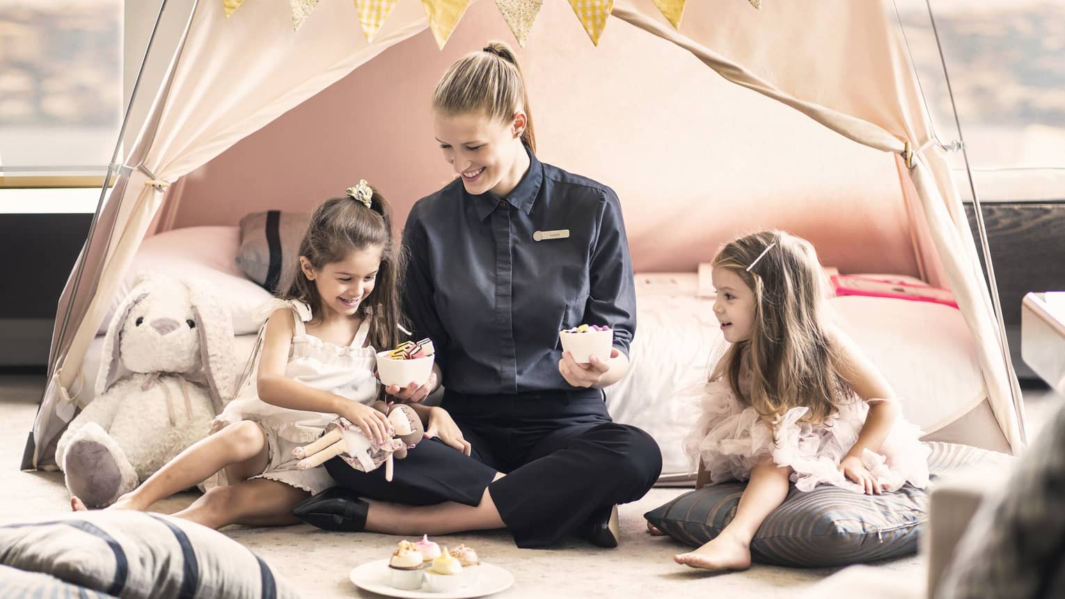 Four Seasons staff member presents two young girls with cupcakes in an in-room tent
