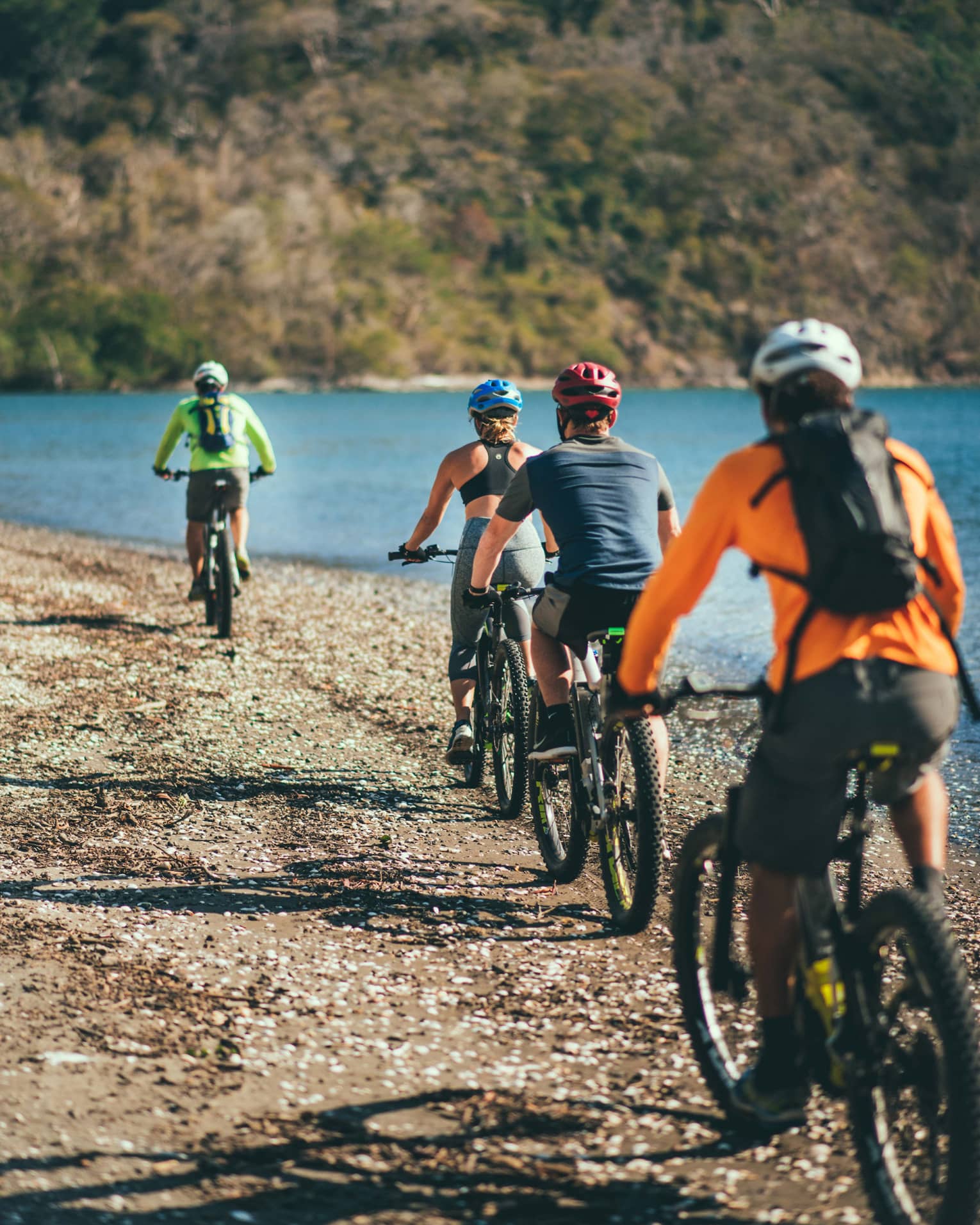 Four people riding bicycles through a rocky terrain next to the ocean