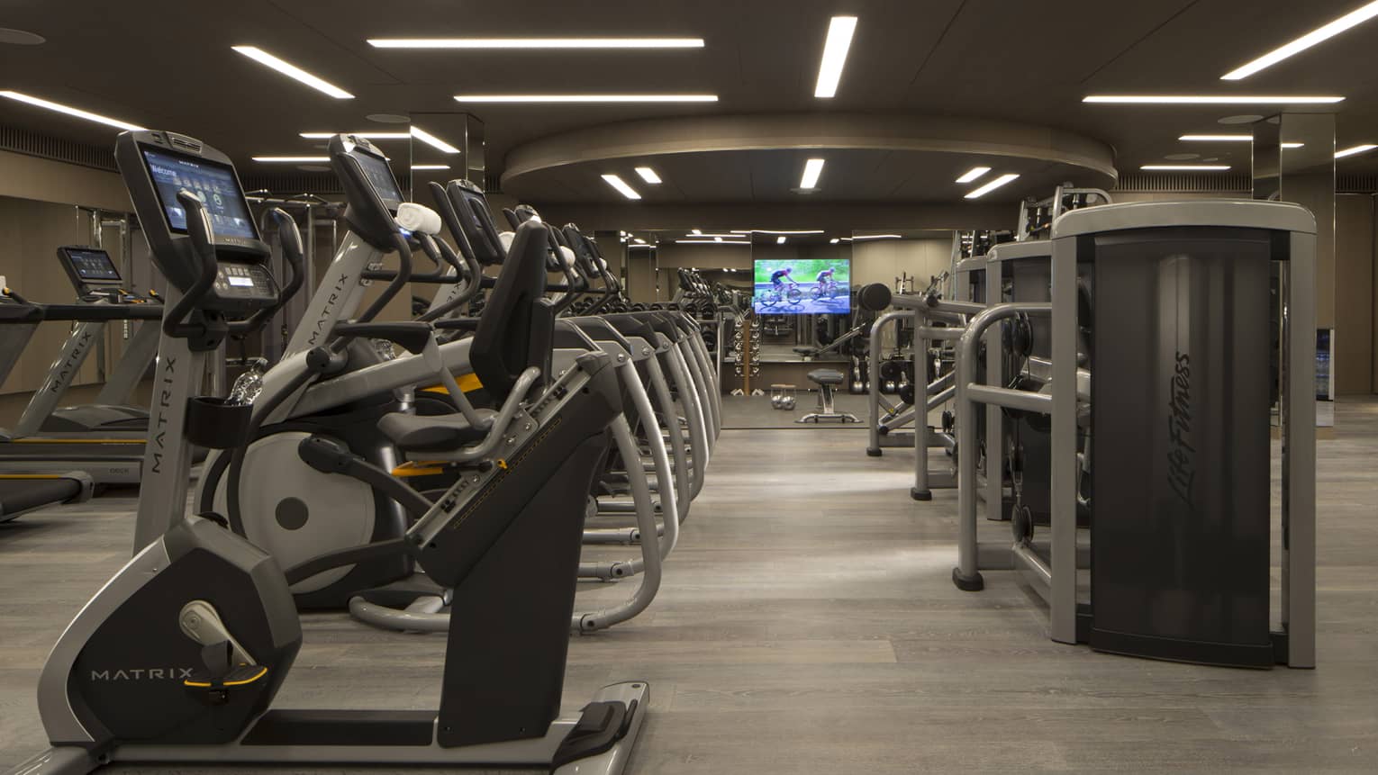 A fully-equipped gym with cardio and weight machines under dim lights.