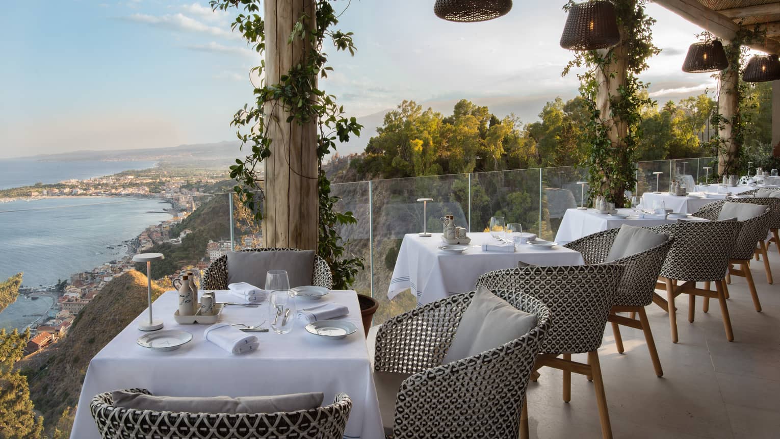 Outdoor restaurant terrace lined with 2-person tables, glass railing and sea view