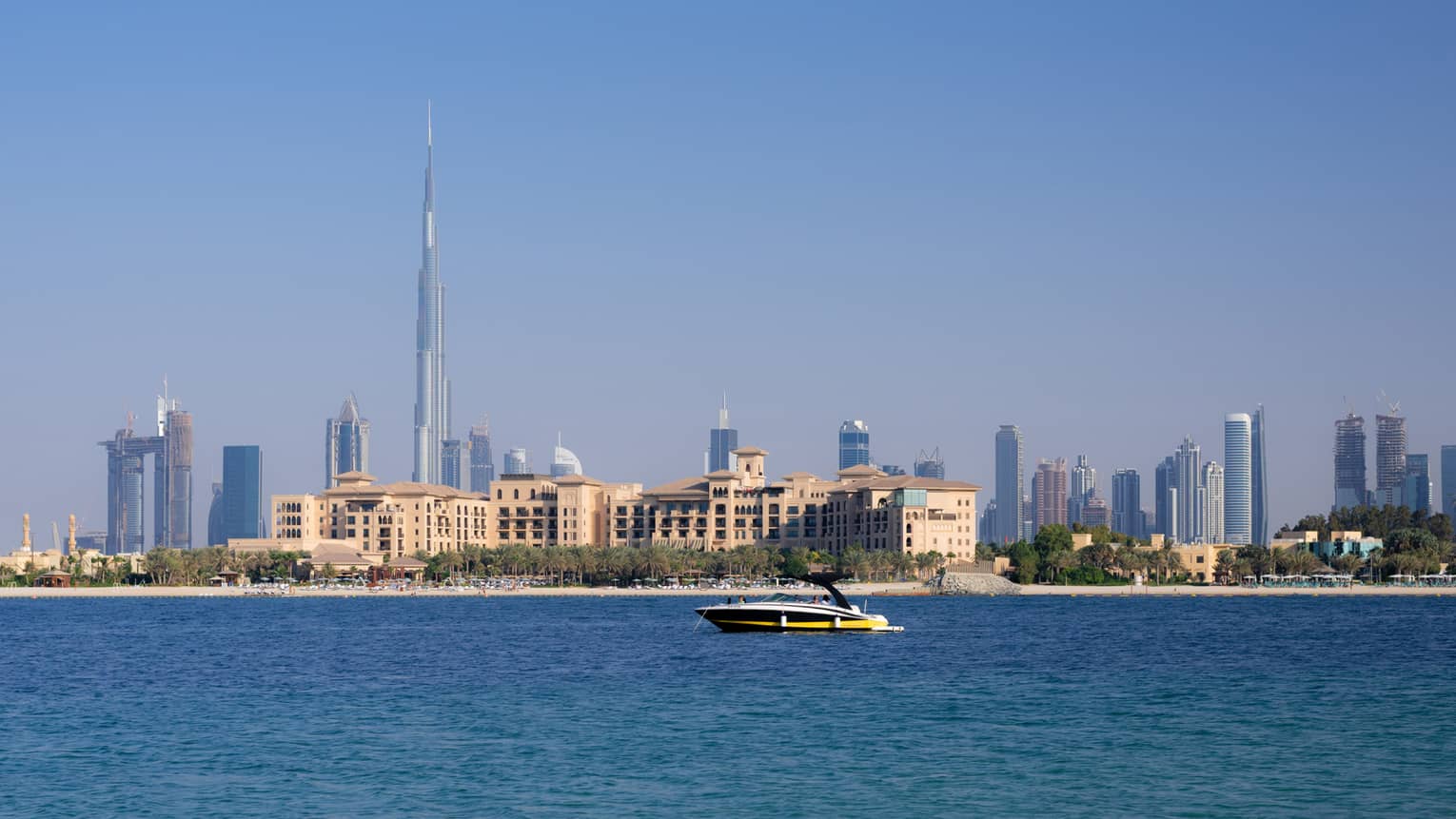 A white, yellow and black speed boat glides through the water with the Dubai skyline in the background