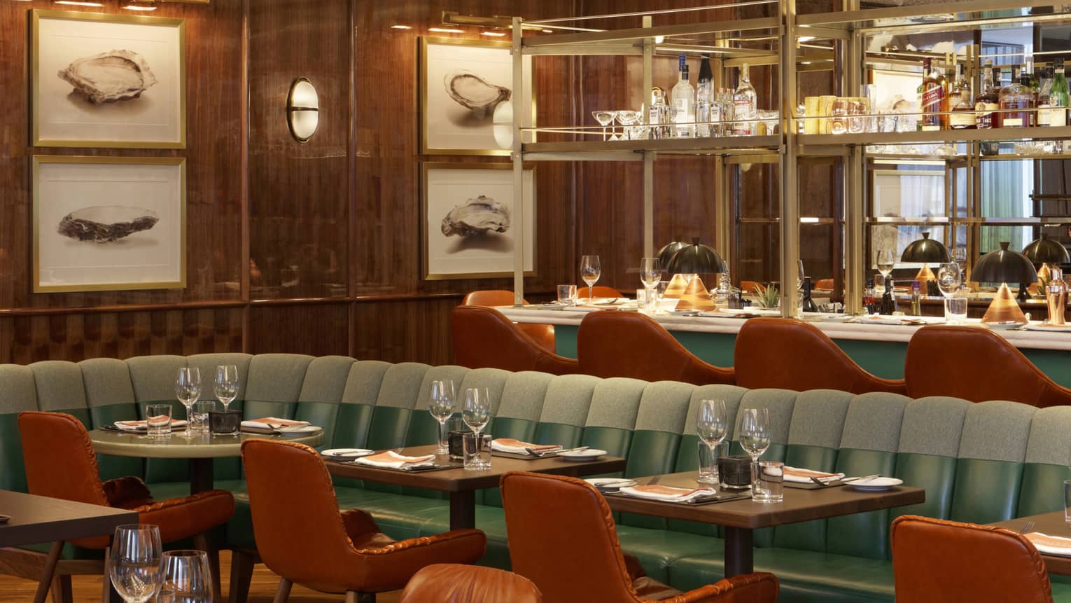 A dining room with burnt orange chairs, and sage green seats framed beneath a mirrored bar, and oak walls.
