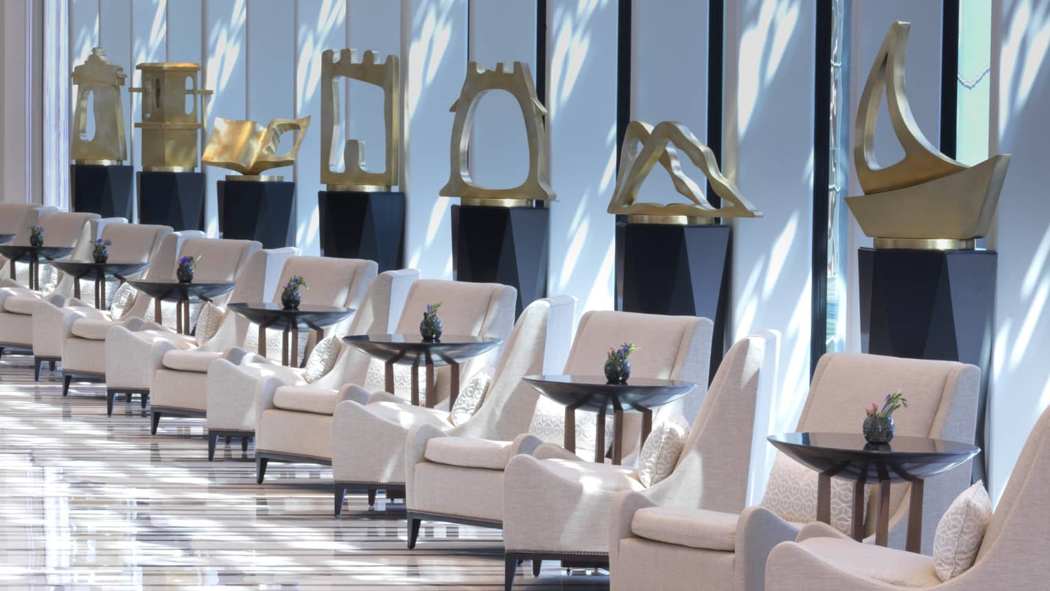 Several golden sculptures are on pedestals in a long white marble hallway. 