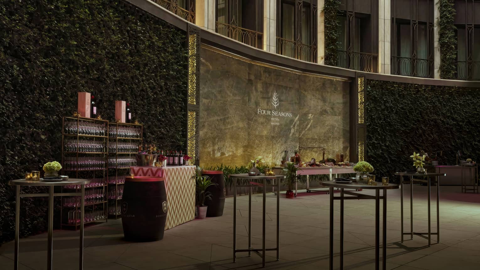 A walled courtyard space with foliage and other plantings, a bar, and several small tables with centerpieces