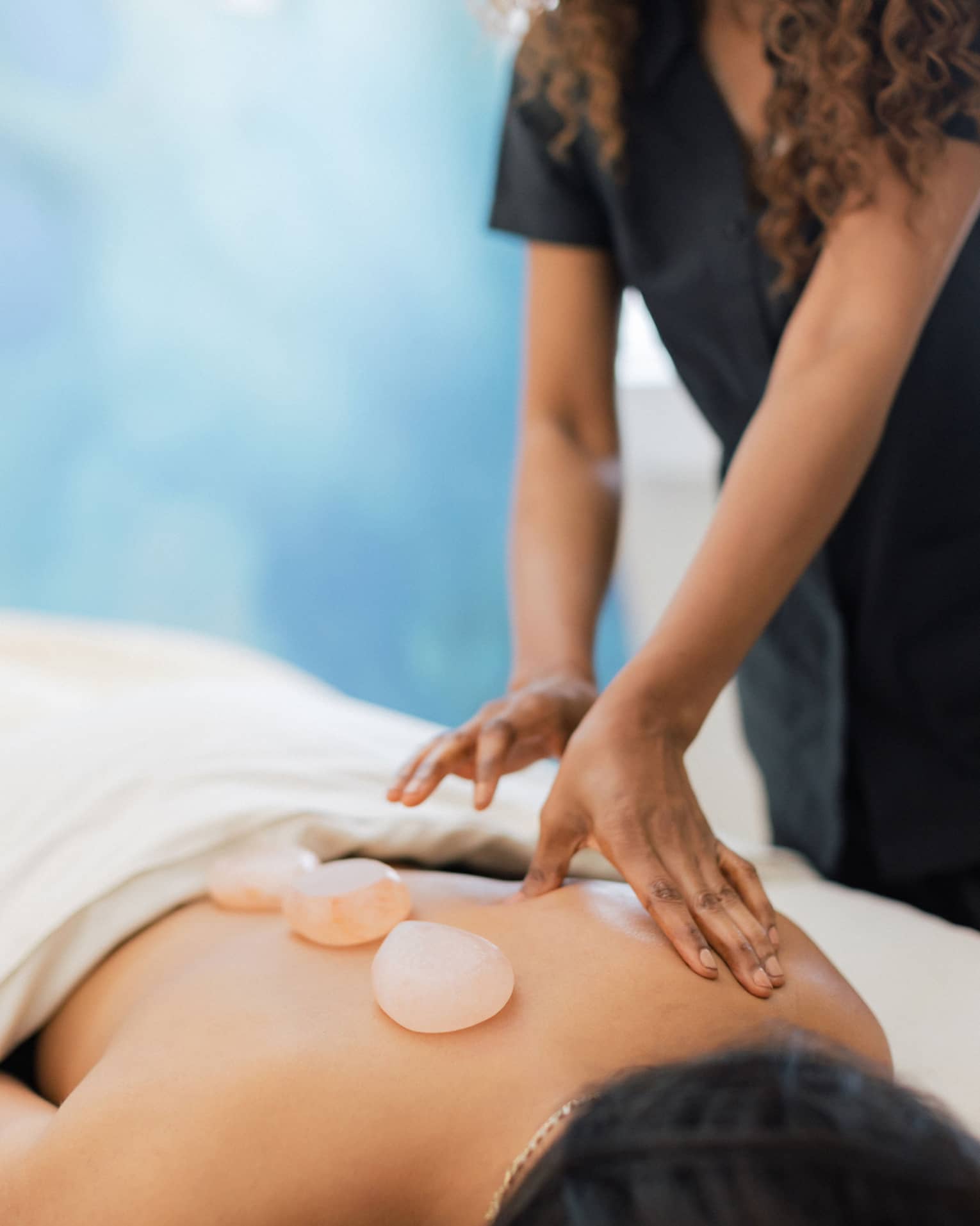 Masseuse places salt stones on a person's bare back