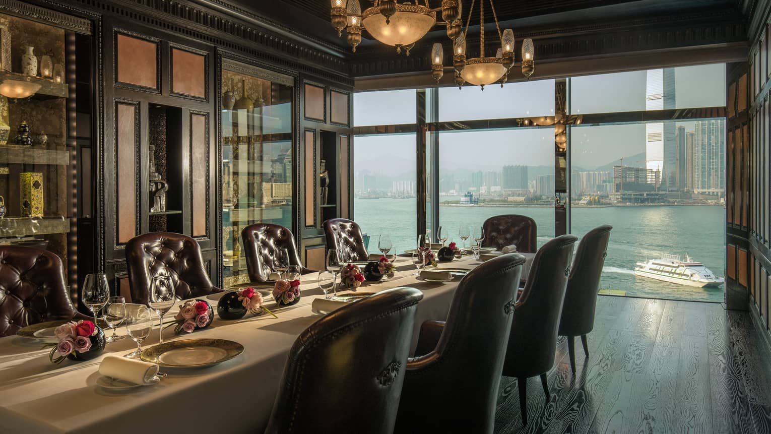 Long private dining table with roses under antique lamps by window overlooking harbour