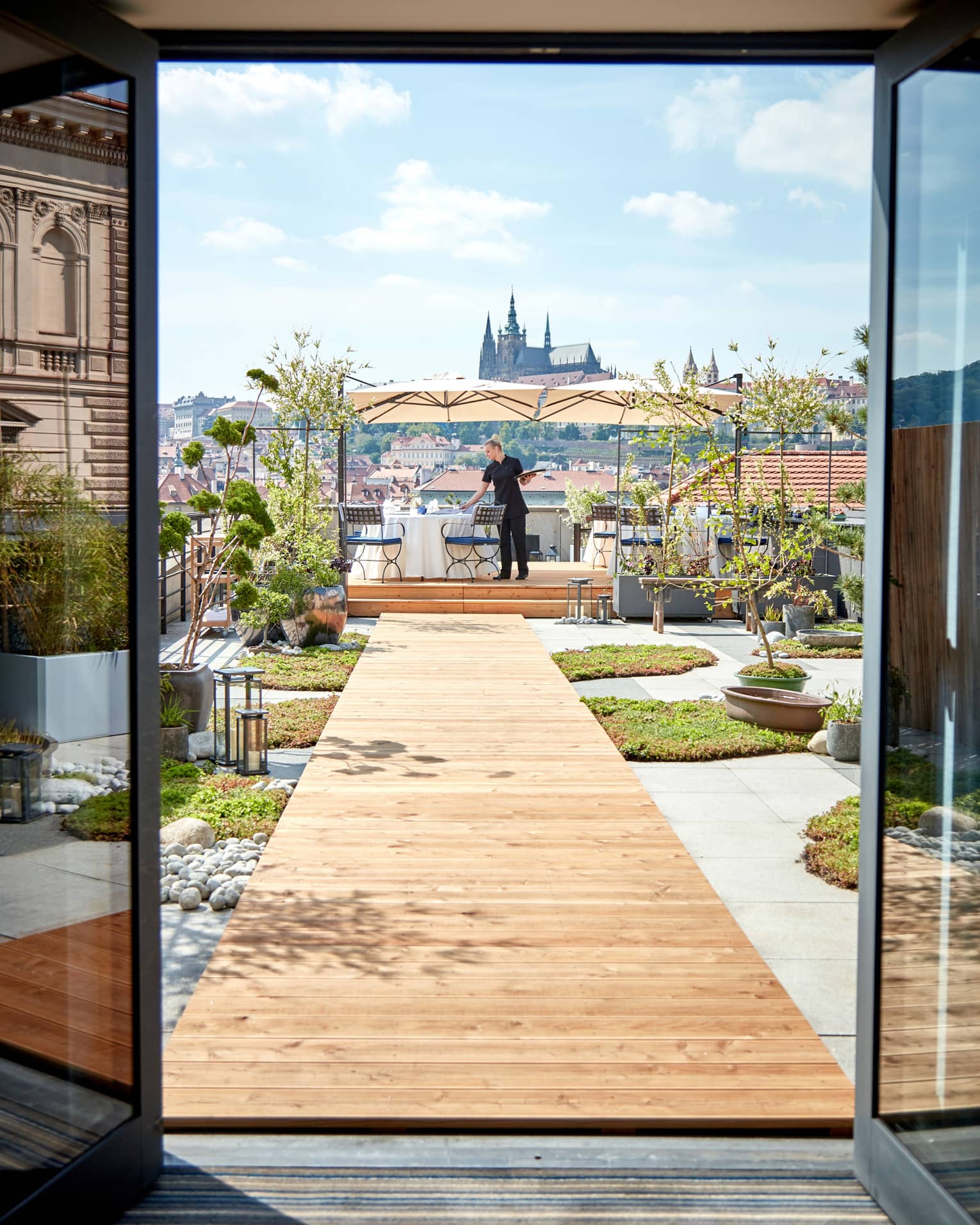 Tall windows looking out to wood plank walkway to server setting table on rooftop MIRU restaurant terrace