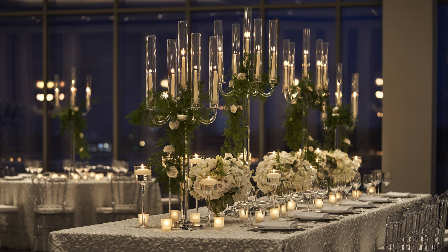 Long tables with table cloth, tall candles, and flowers.