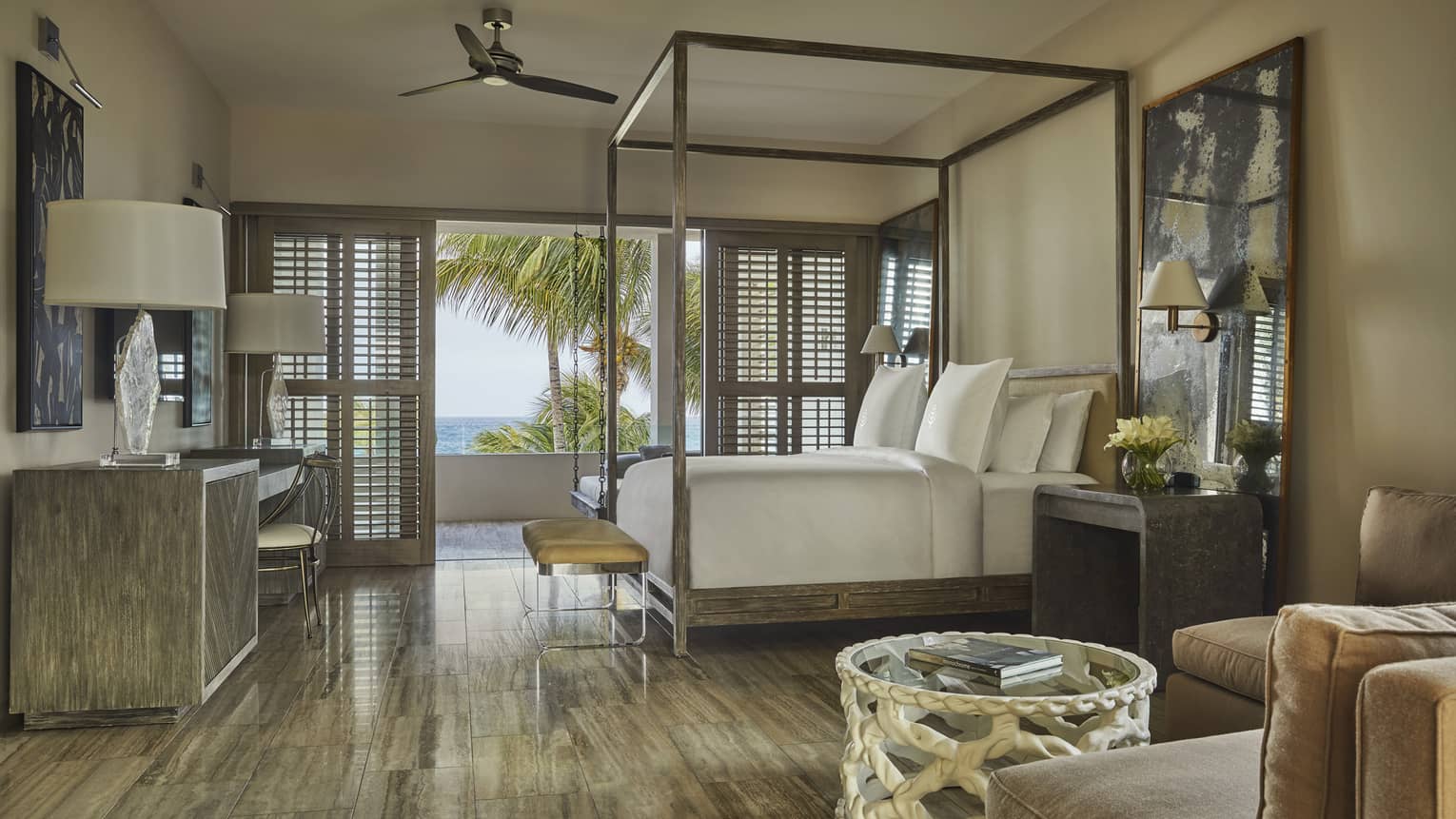 Luxury villa bedroom with a canopy bed, elegant decor, large windows with shutters and a balcony offering ocean and palm tree views