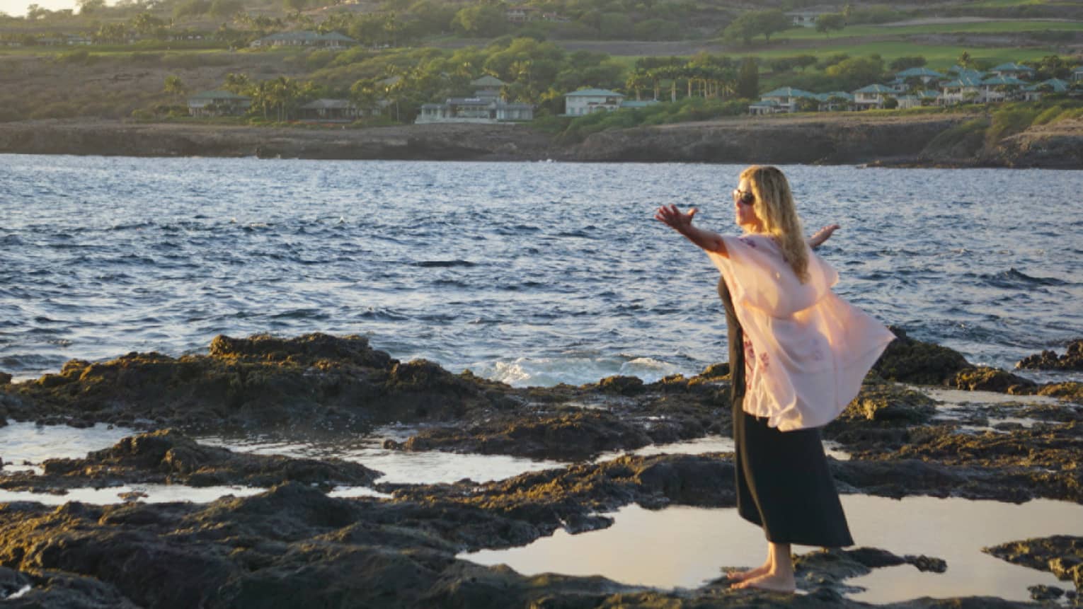 A woman meditates at edge of ocean on lava rock