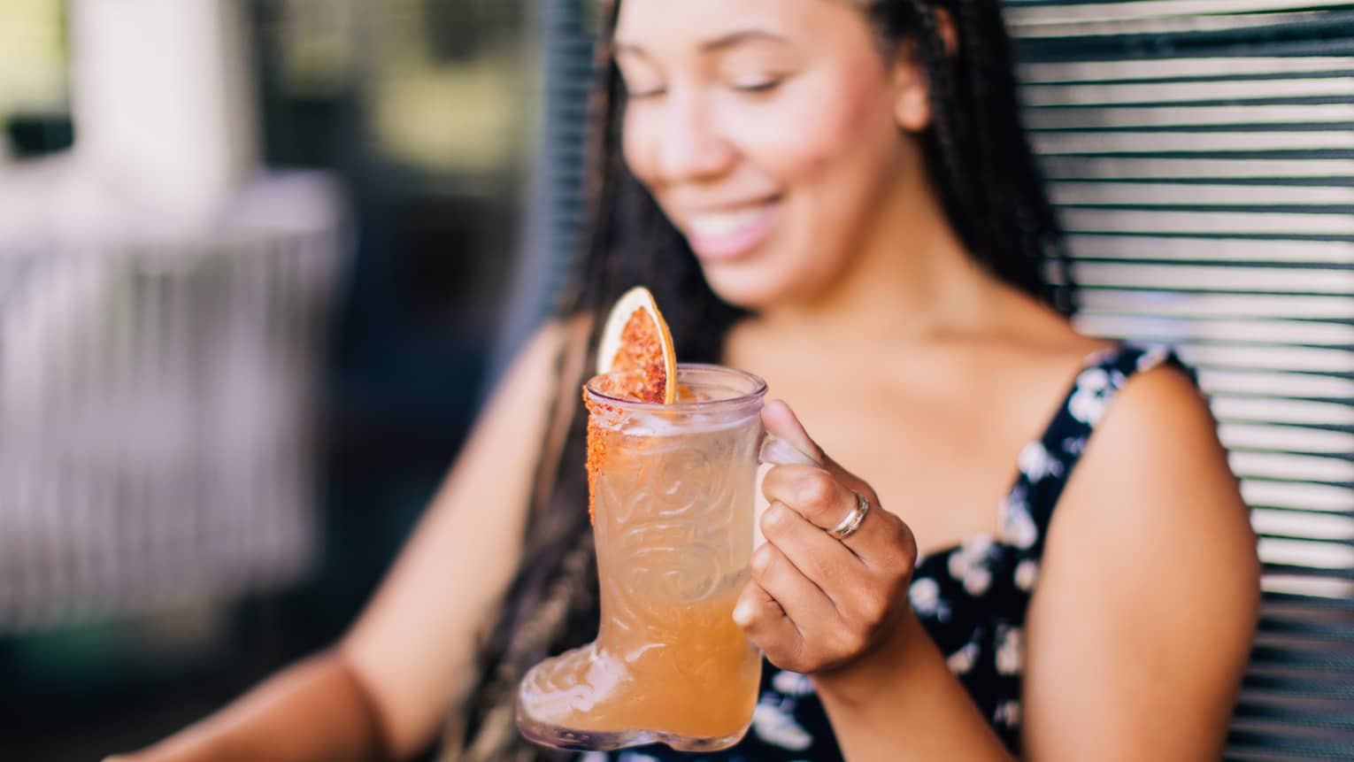 A woman in a black dress drinking an orange coloured cocktail.