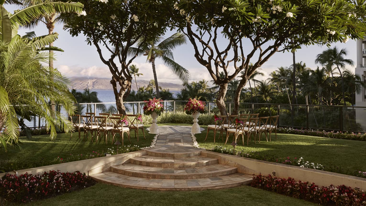 Outdoor wedding with chairs, flowers facing towards ocean and island, surrounded by trees 