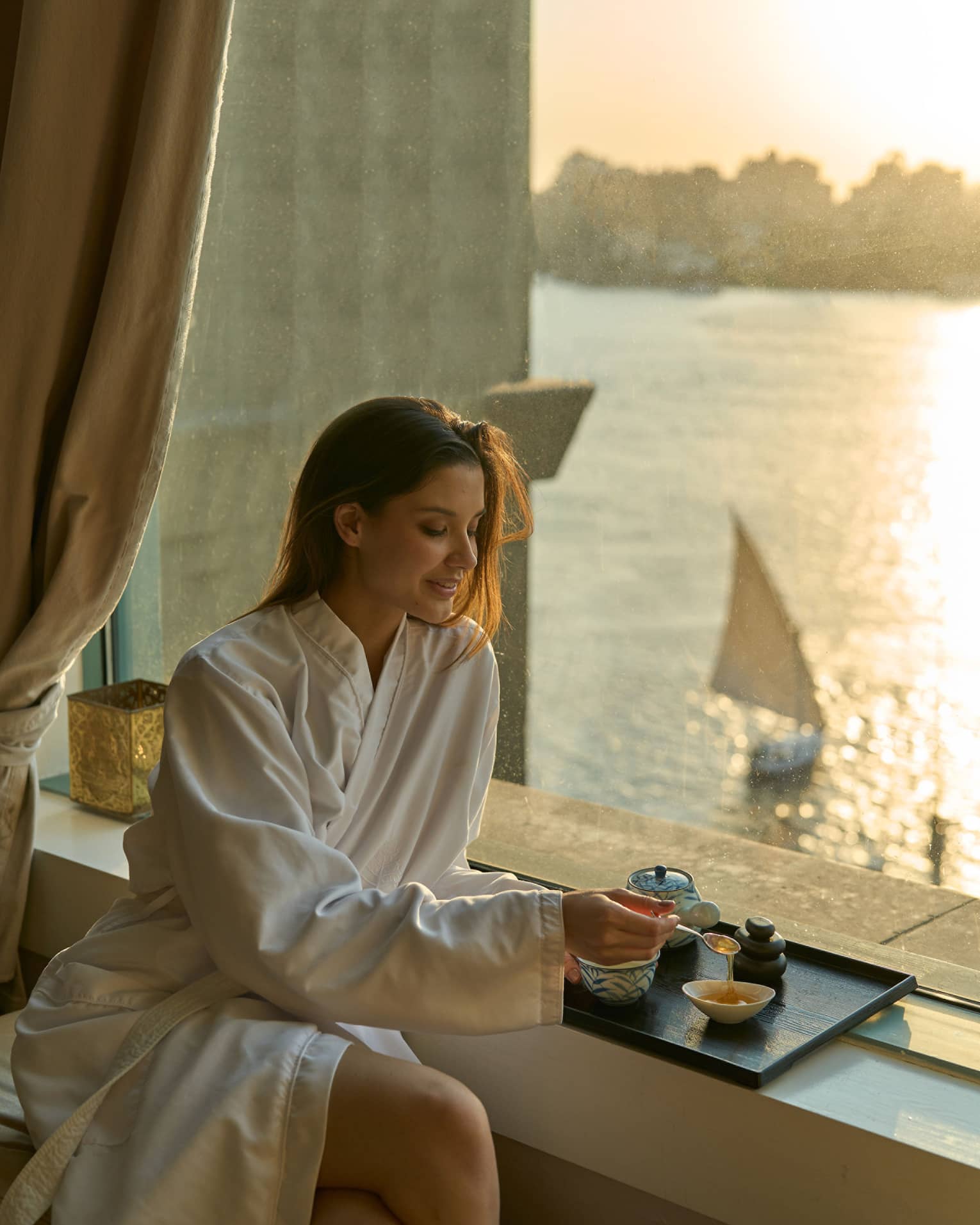 Woman in Four Seasons robe enjoys tea by the window at sunset