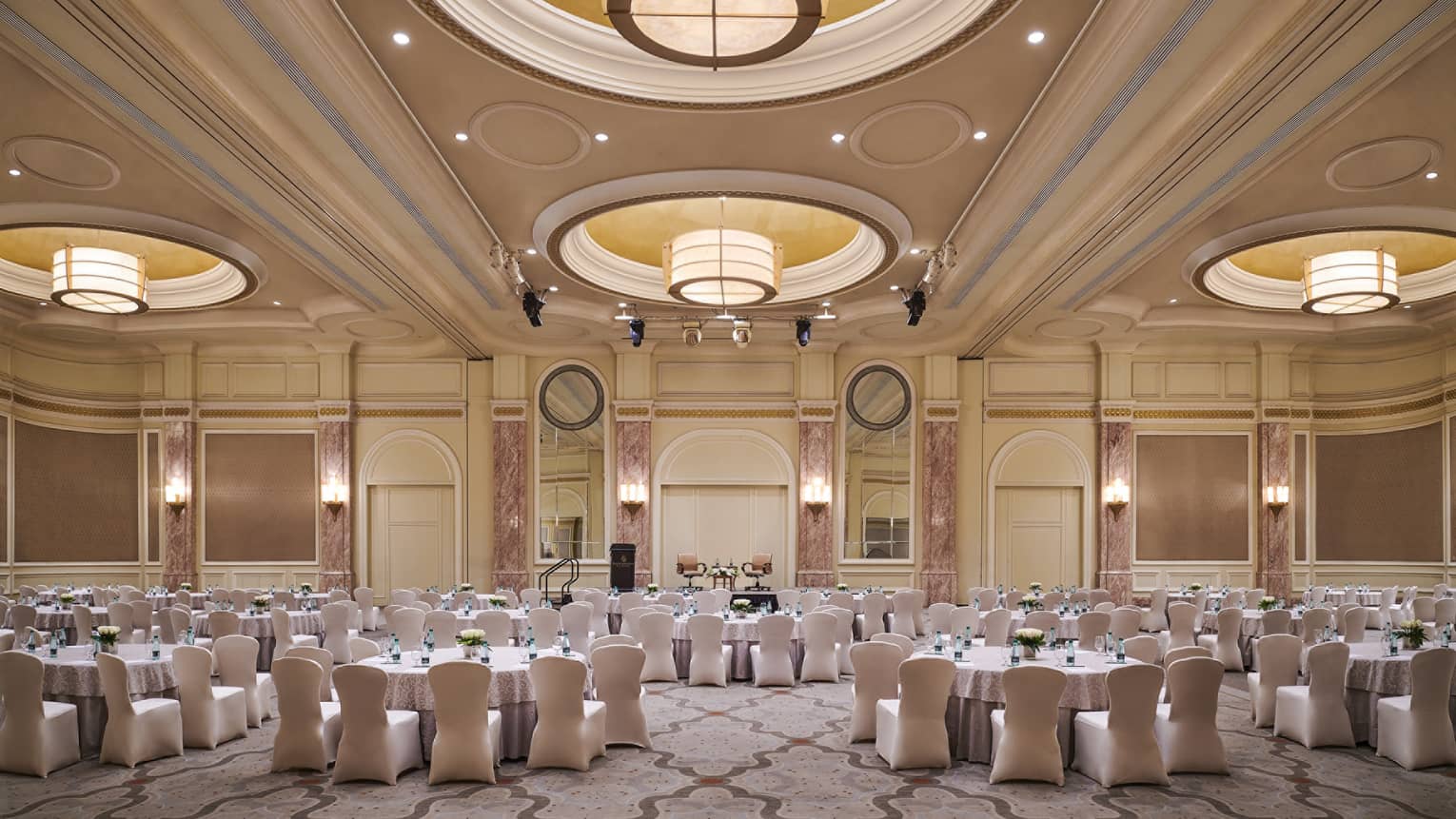 Round dining tables in large ballroom with recessed domes, large lights along high ceilings 