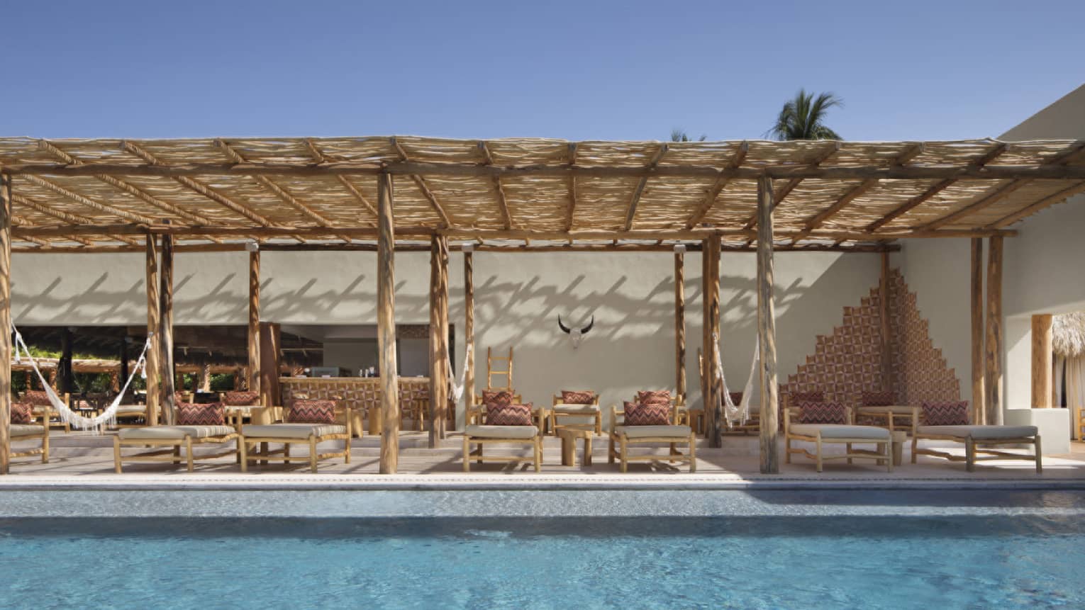 Outdoor pool with bamboo lounge chairs under thatched roof awning