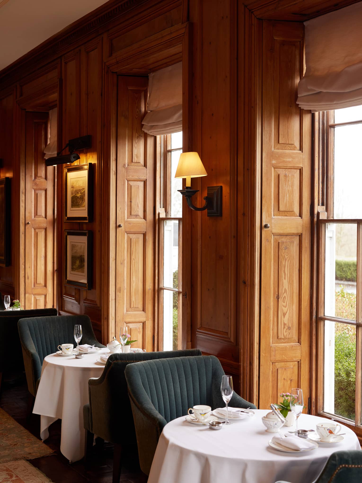 Cosy lounge with wood-panelled walls and small round tables and chairs by tall windows