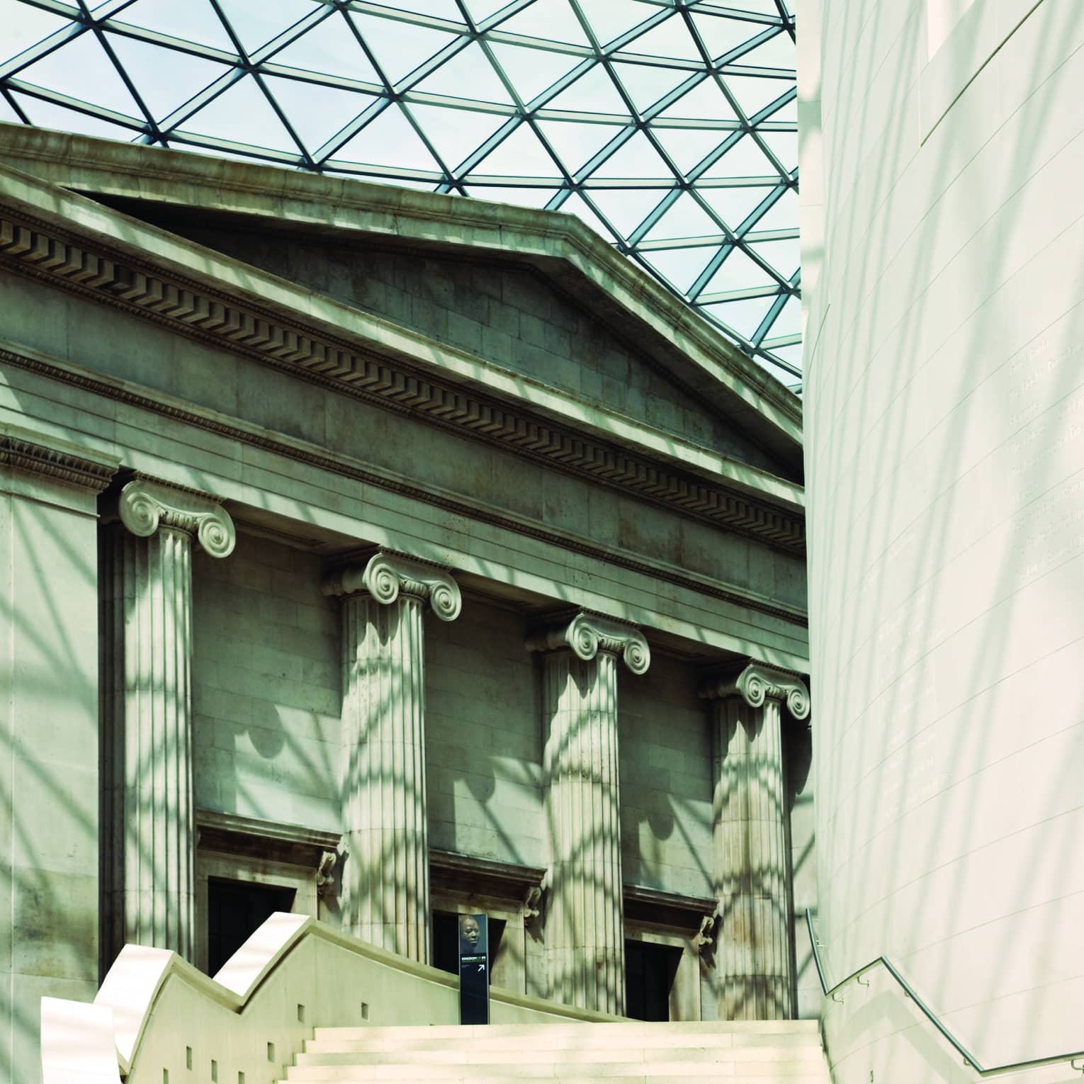 Close-up of façade and staircase in the British Museum courtyard, light through the glass roof leaving criss-cross shadows.