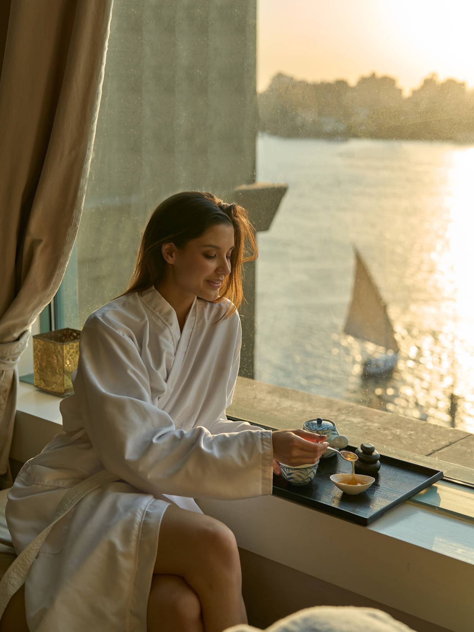 Woman in Four Seasons robe enjoys tea by the window at sunset