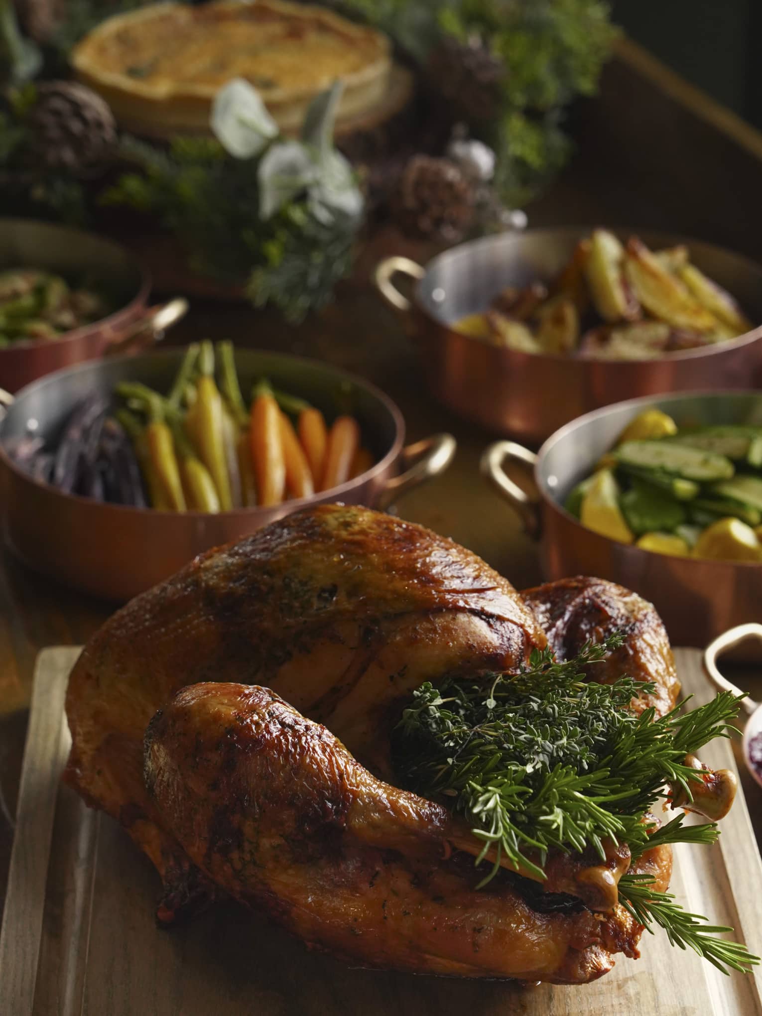 Festive turkey stuffed with rosemary on carving board, accompaniments and side dishes in the background