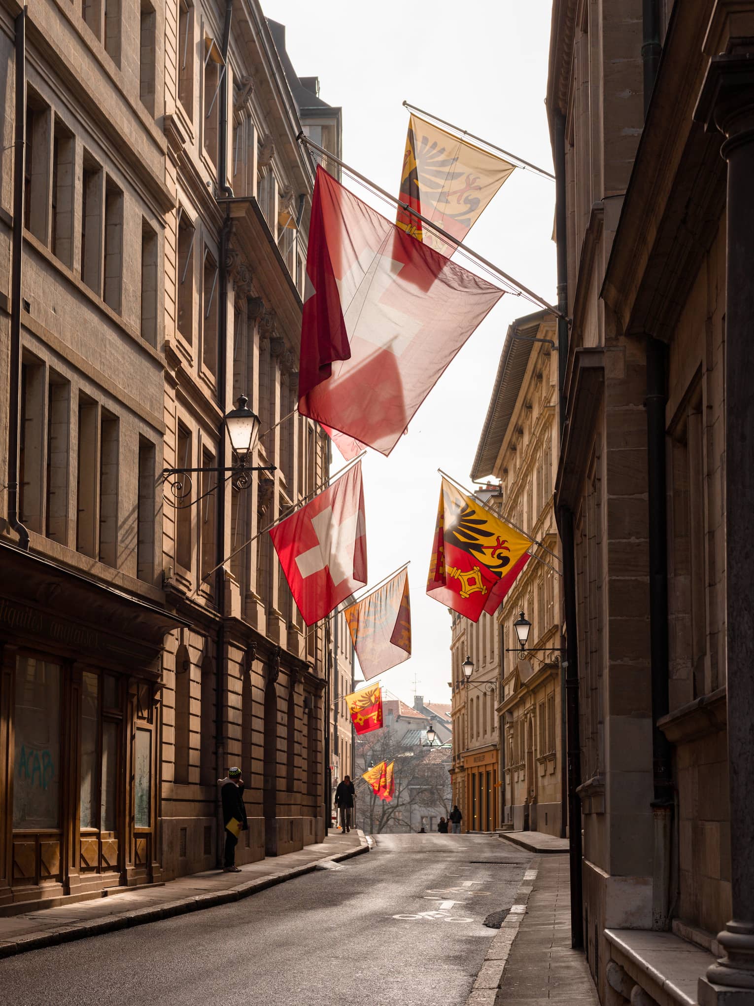 Narrow street in Old Town Geneva lined by Swiss flags hanging from the walls of the traditional buildings. 