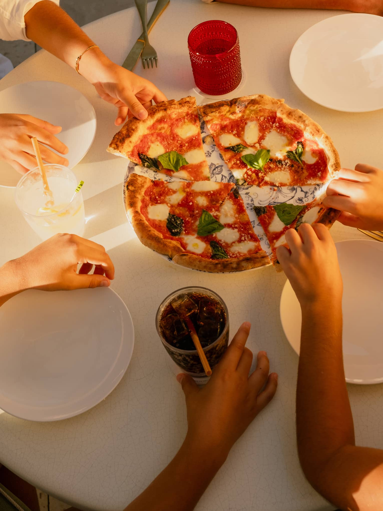 Four people sit around a table reaching in for a pizza set in the centre