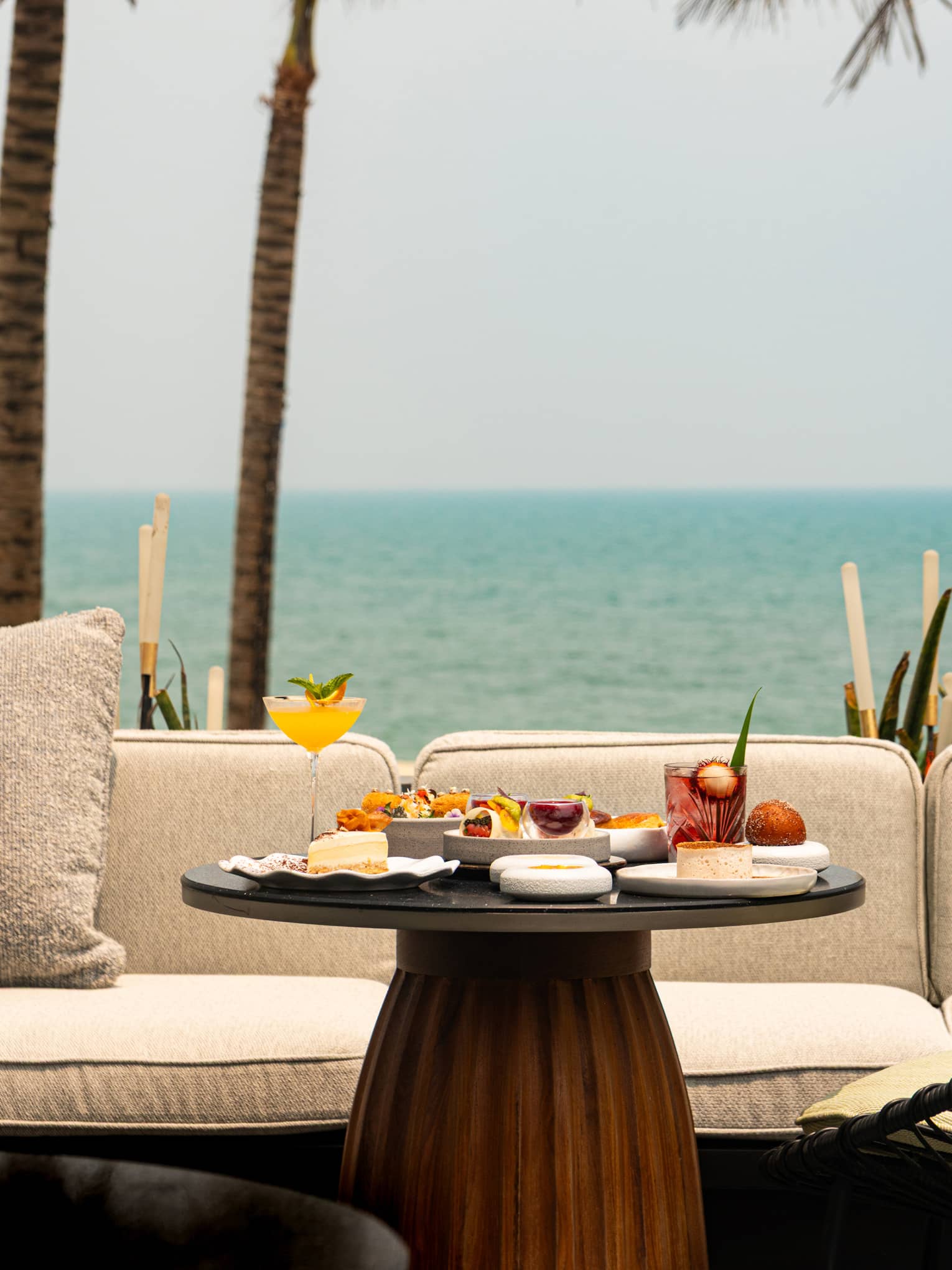 Round table set for afternoon tea in front of cream outdoor sofa, overlooking the sea