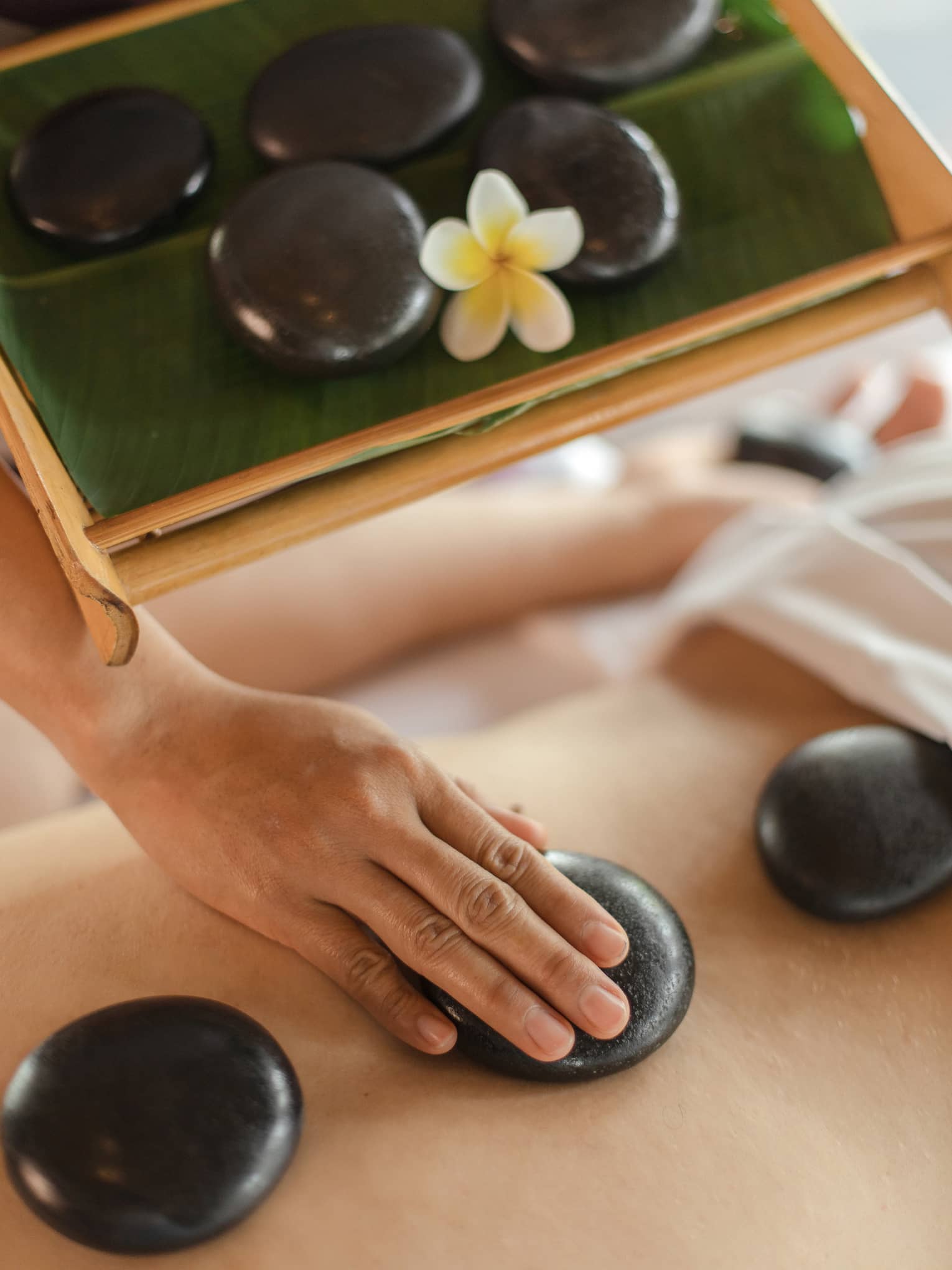 A pair of hands places three massage stones on a client's back, while also carrying a tray of more stones