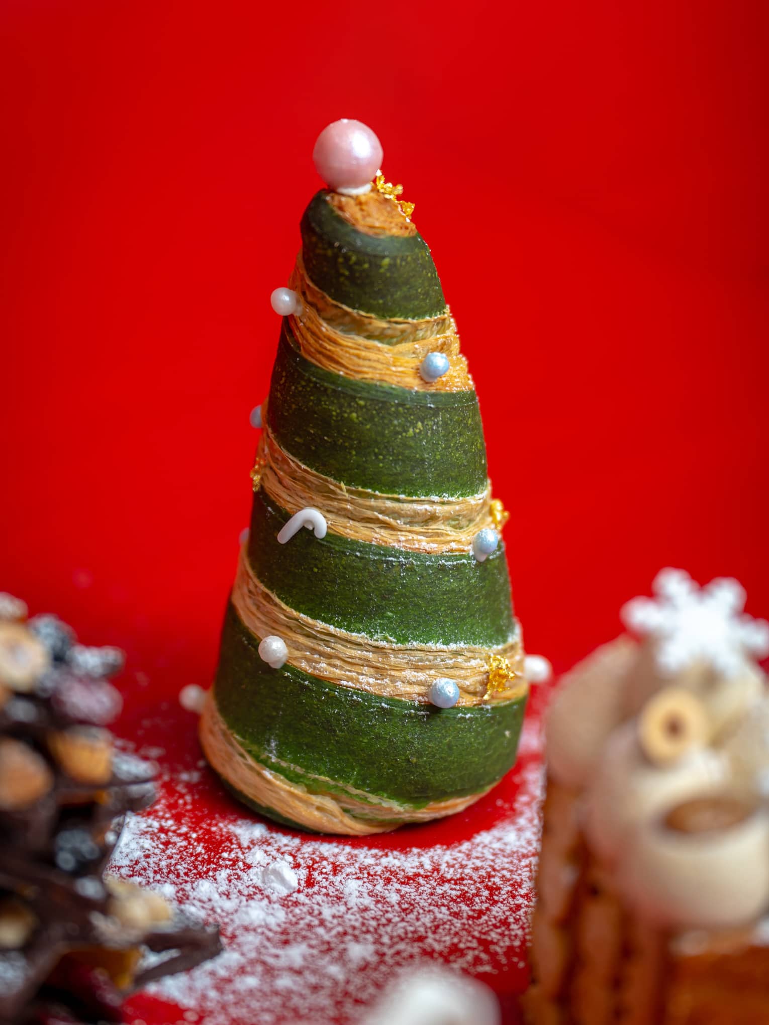 Green Christmas tree–shaped pastry with gold accents on red background