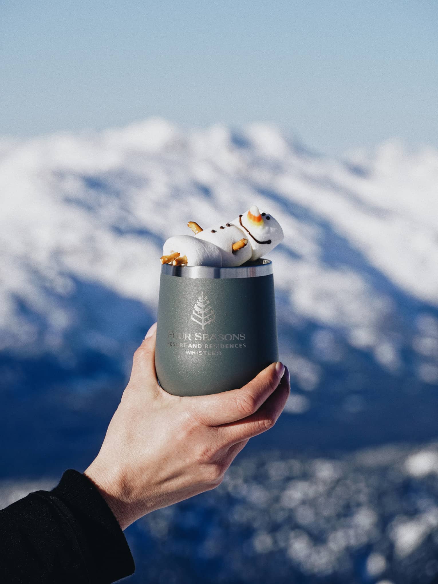 Hand holding a blue mug filled with hot chocolate in front of a snow-covered mountain