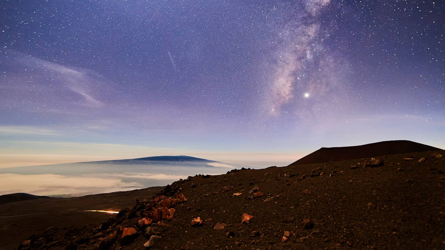 Sunrise under starry sky above mountain, volcanic rocks