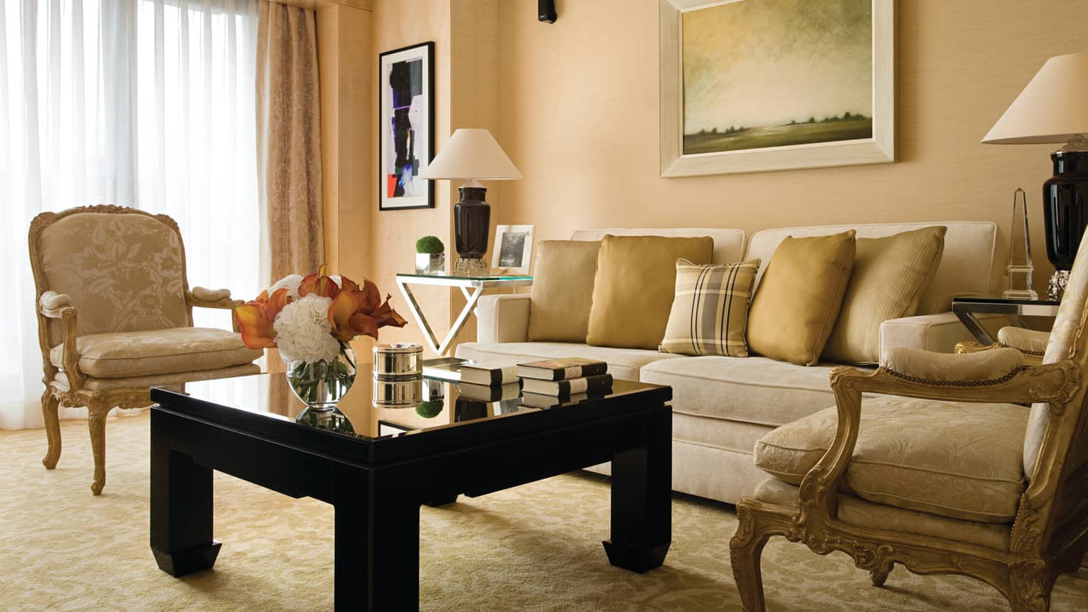 One-bedroom Suite living room with gold accent chairs, flowers and books on black coffee table