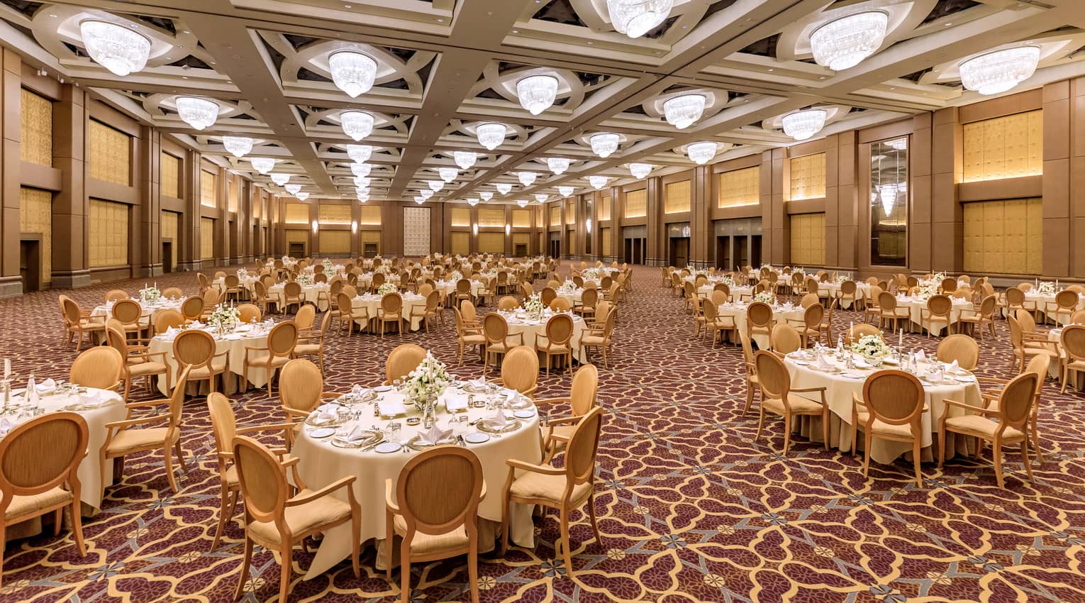 Grand ballroom with banquet tables set for event. Patterned carpeting and ceiling with squares of lights.