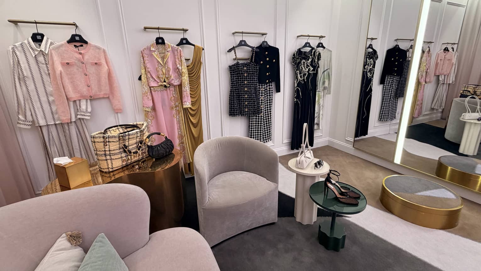 Large dressing room with arm chairs and tables and various curated outfts hung on the wall