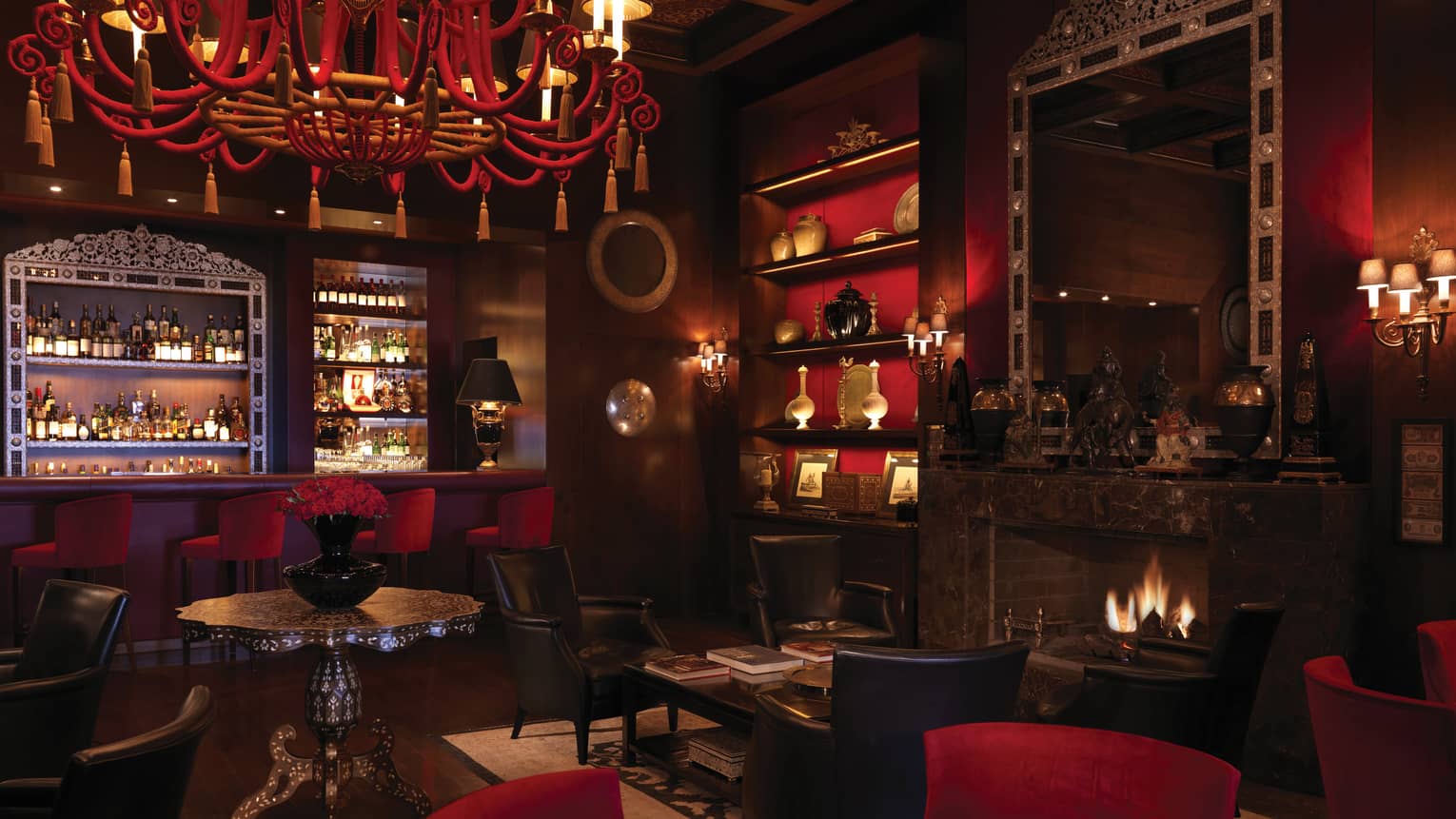 Bar interior with dark wood, red chandelier, shelf and velvet bar stools, arabesque ceiling, fireplace